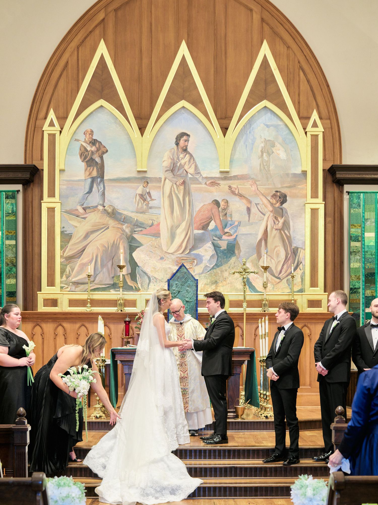 Bride and groom share a kiss at the altar of a stunning church with a beautiful religious mural backdrop during wedding ceremony.