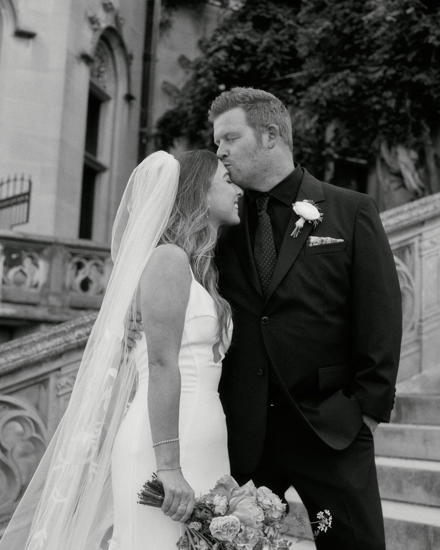A bride and groom share an intimate moment on stone steps in black and white photography.
