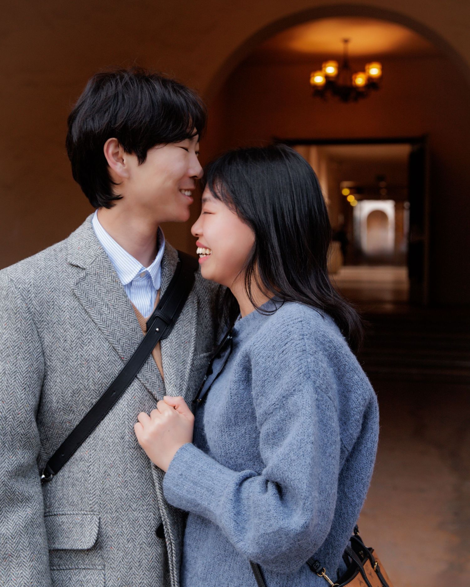 Couple in winter coats sharing tender moments in covered walkway.