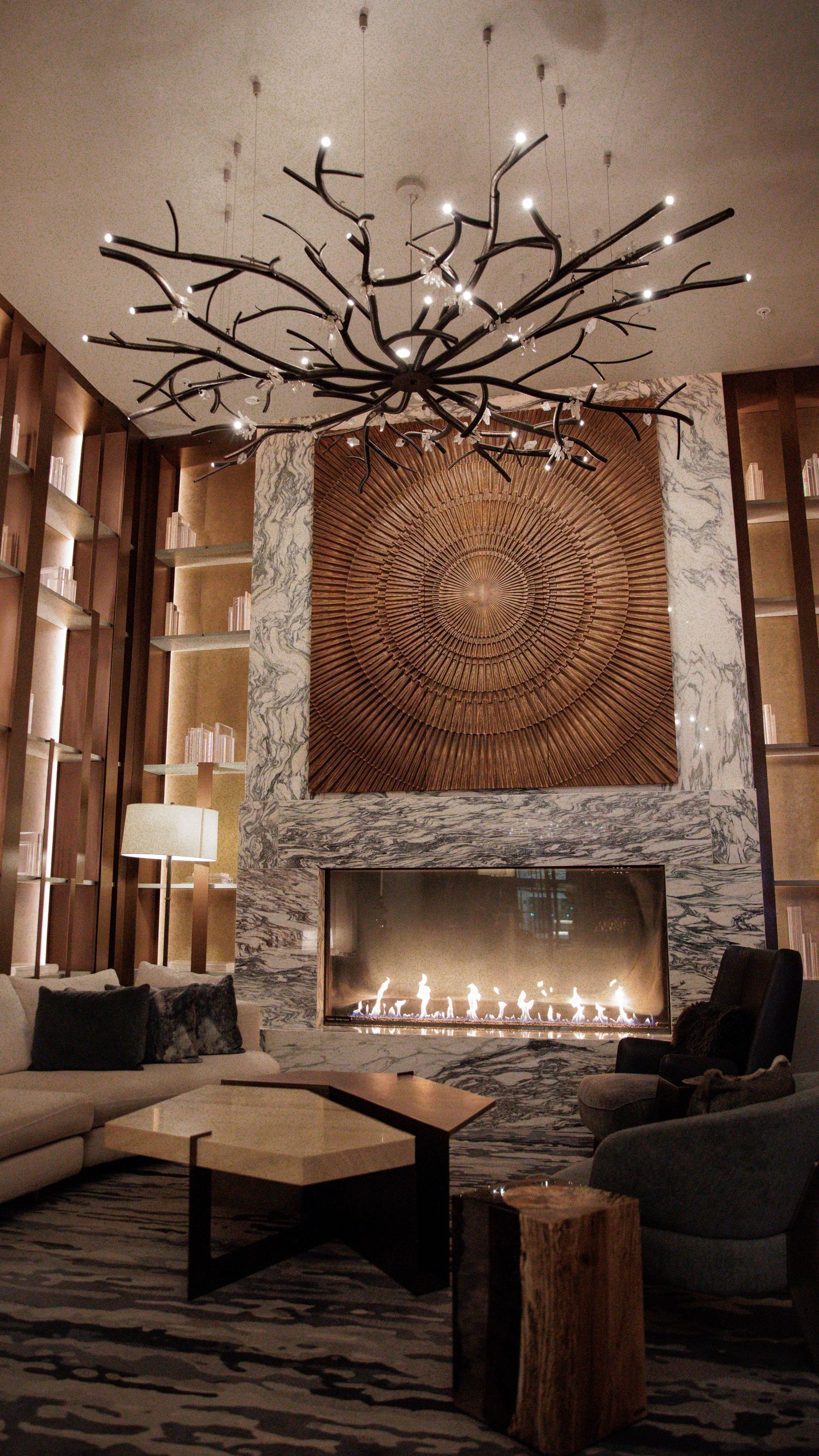 Modern lounge area with stone walls, branch chandelier, and linear fireplace creating a cozy ambiance.
