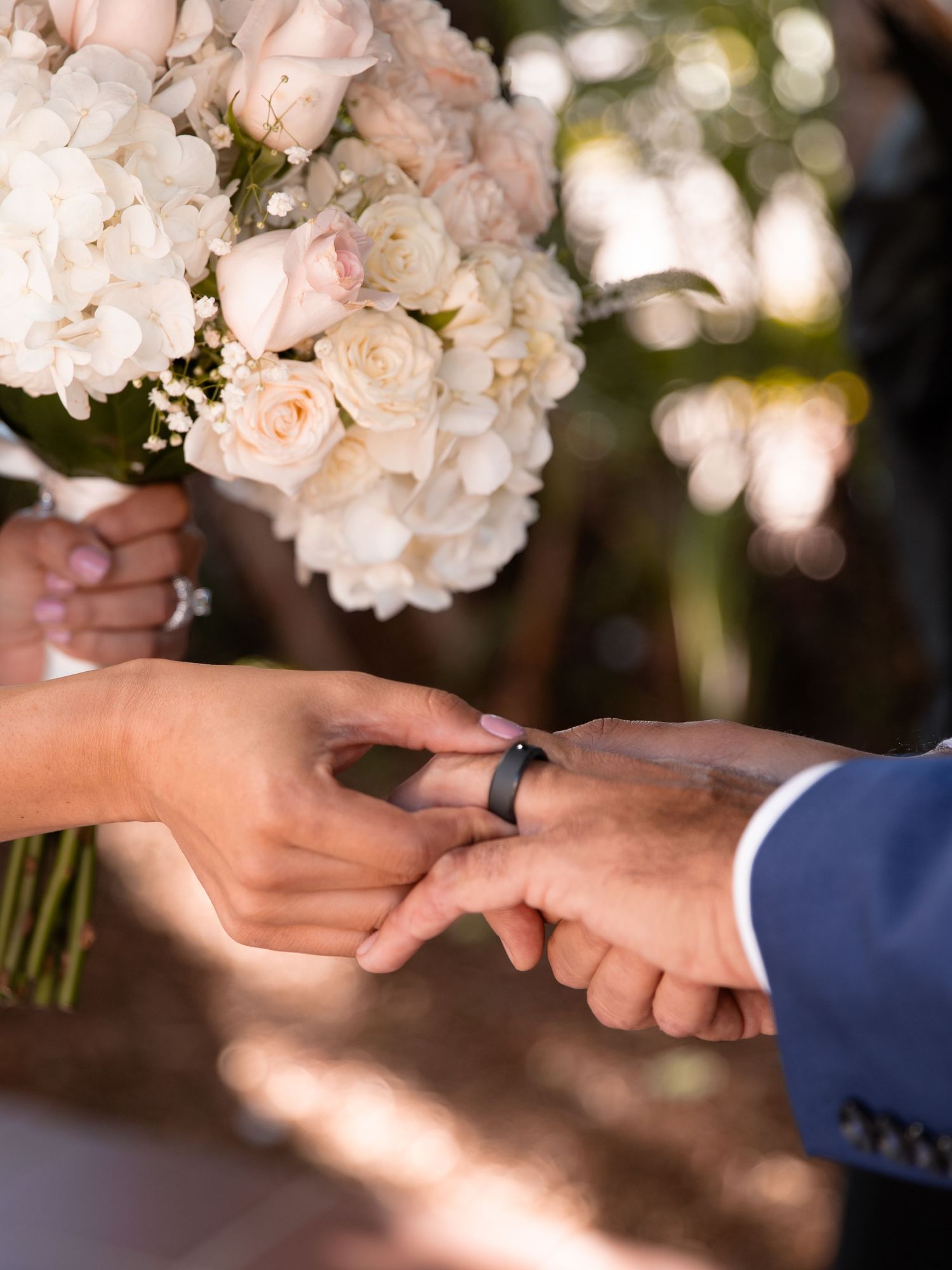 Delicate white rose bouquet and wedding ring exchange in soft natural lighting.
