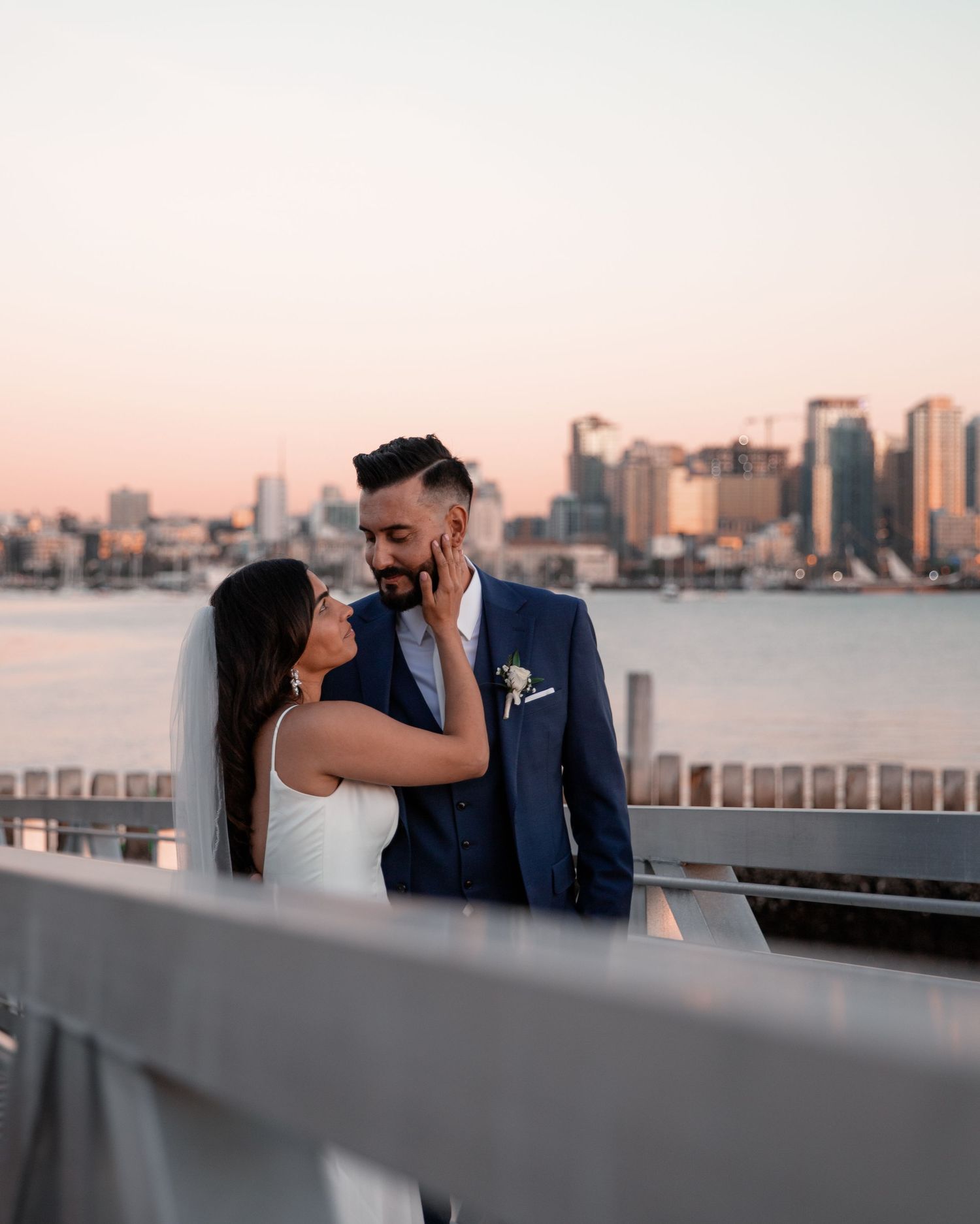 A couple shares a romantic kiss at sunset with the San Diego skyline and harbor visible in the background.