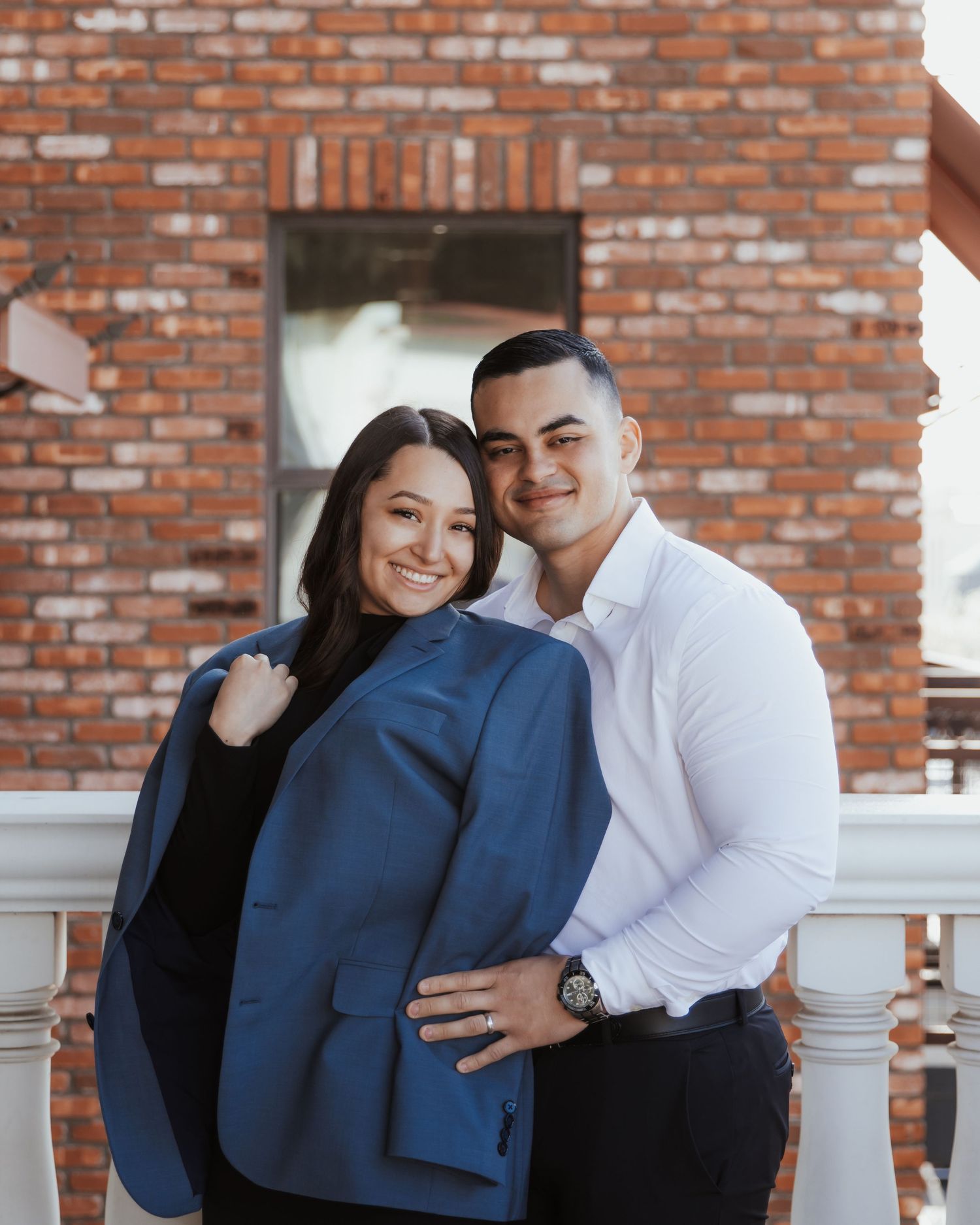 Couple sharing intimate moments against a rustic brick wall background in a casual photoshoot.