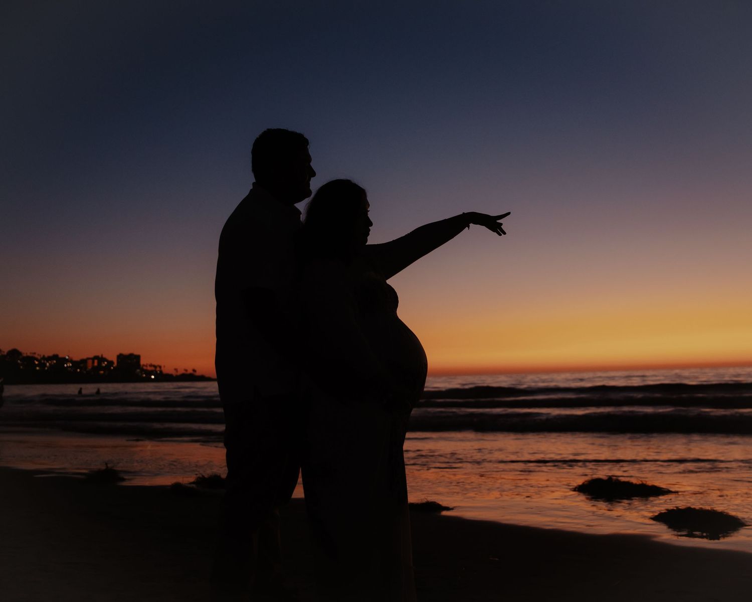 Silhouetted figures against dramatic sunset sky over water.