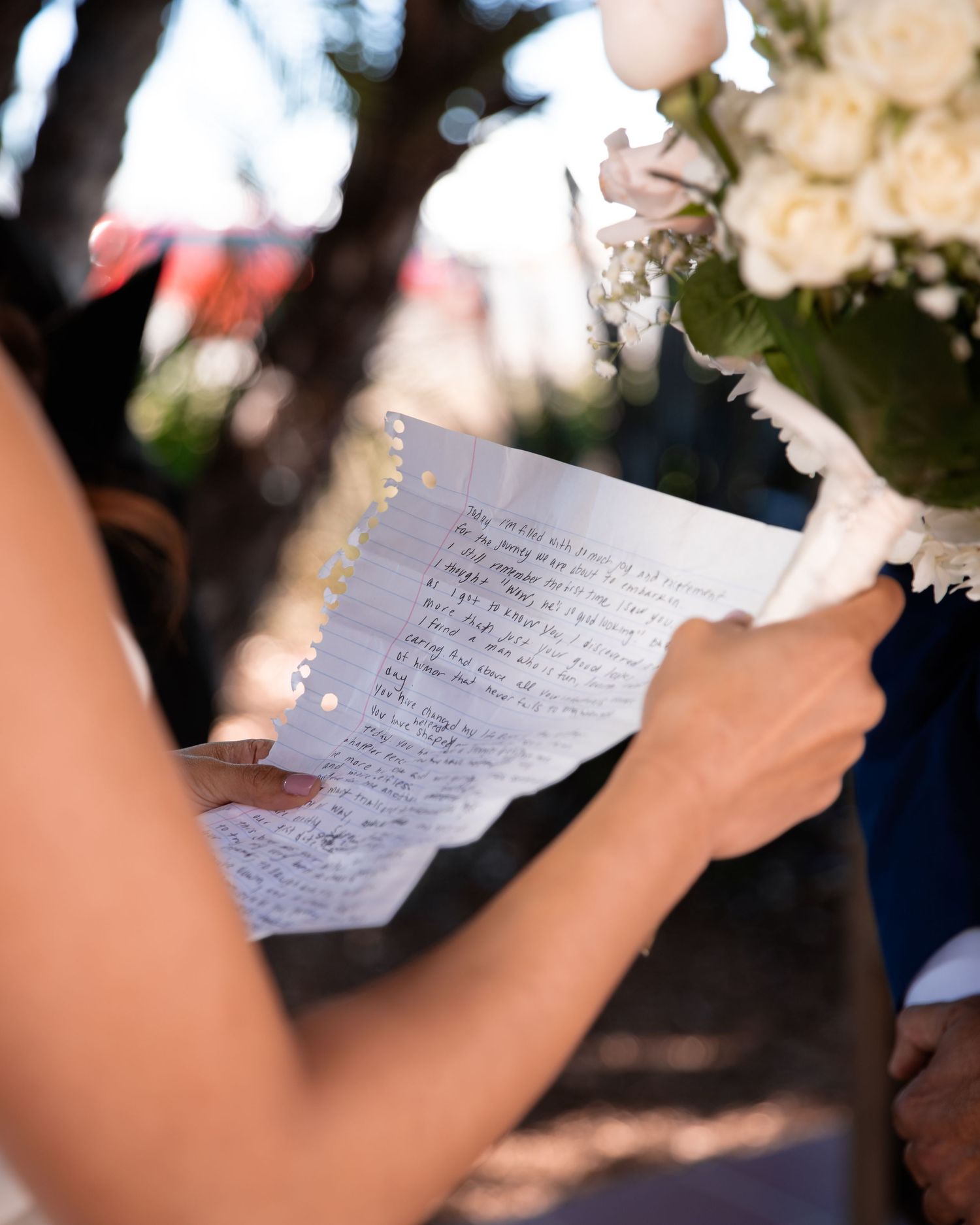 Close-up of handwritten wedding vows on paper with white floral bouquet.