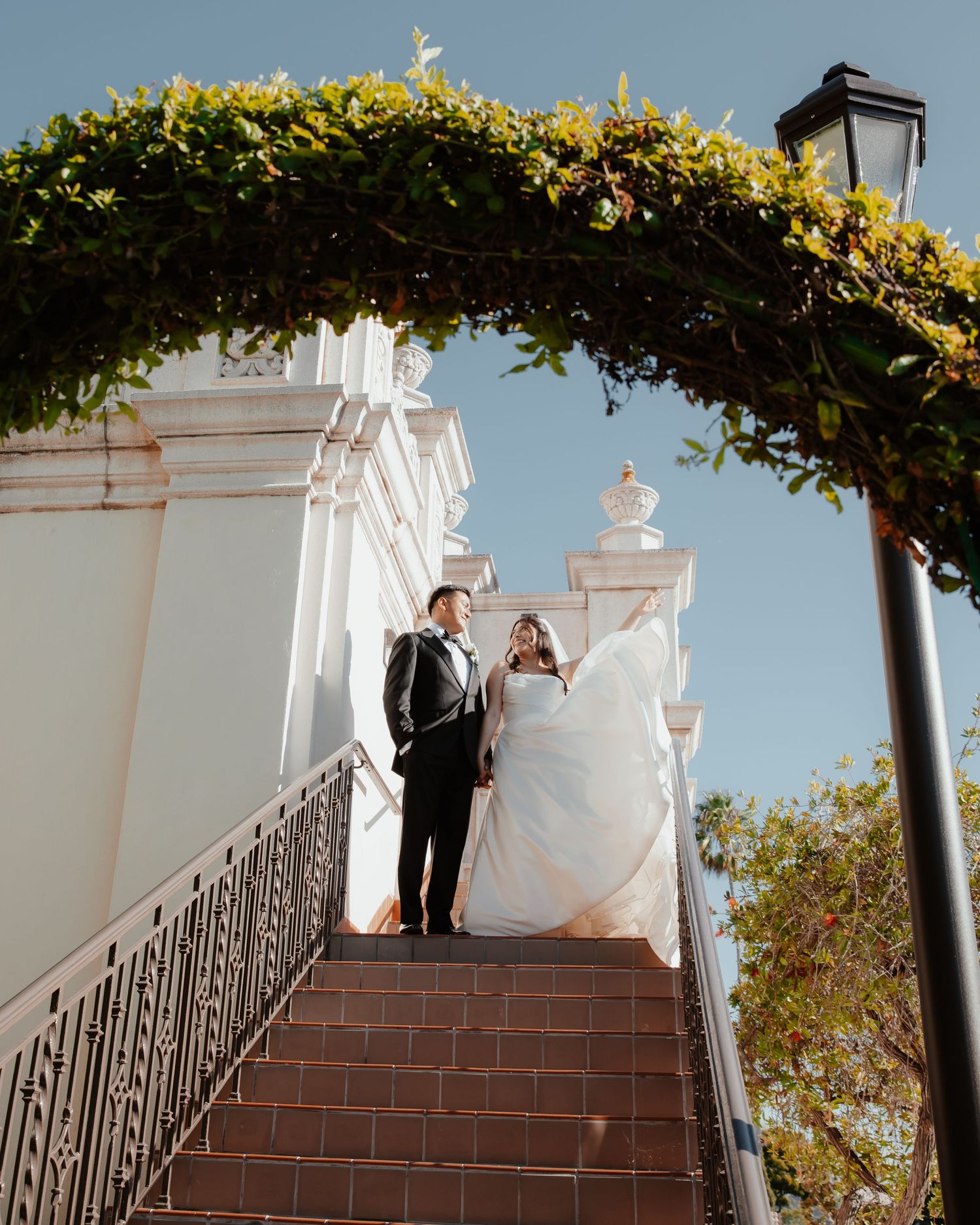 Couple ascending outdoor brick stairs under a lush green archway at a wedding venue.