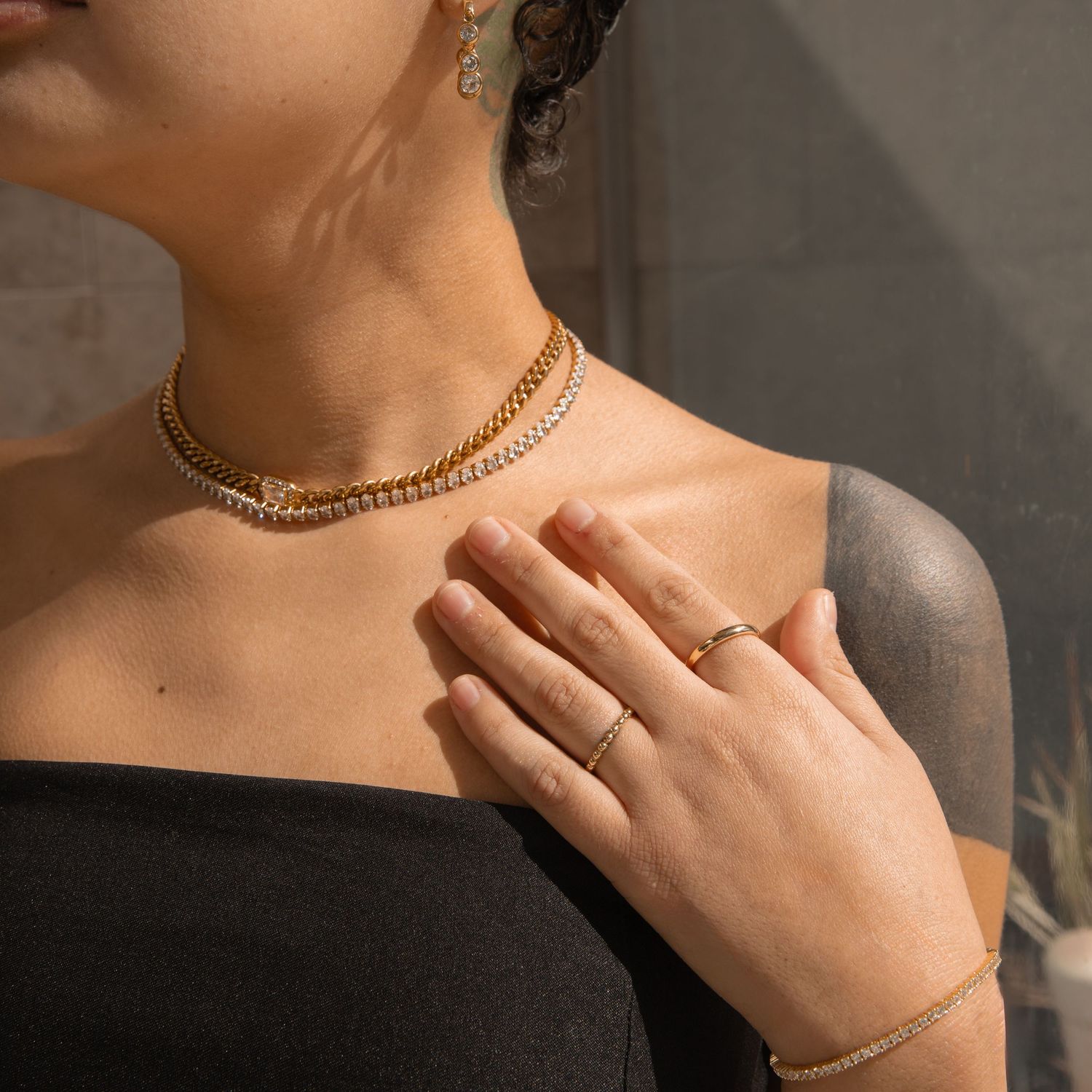 Close-up of layered gold necklaces and rings on person wearing black top.