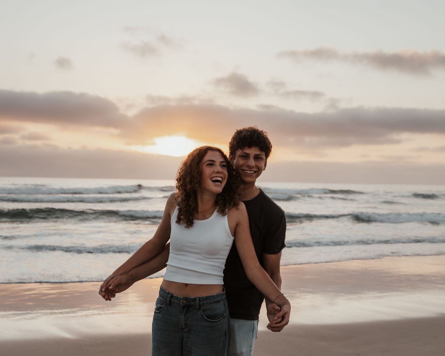 Joyful couple laughing and embracing on beach at sunset.