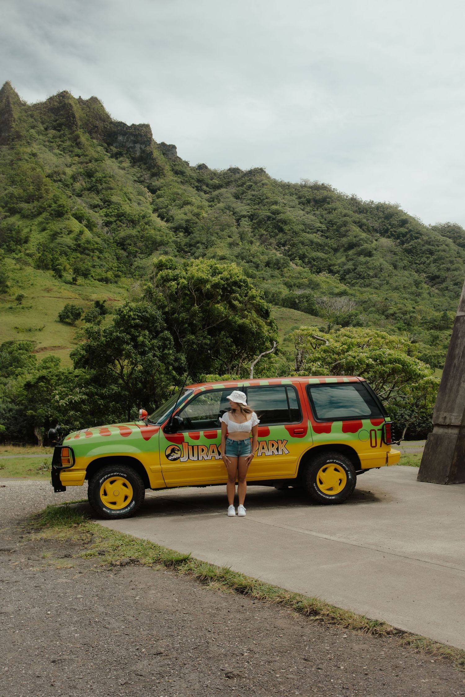 Colorful Jurassic Park themed tour vehicle parked against lush mountain backdrop.