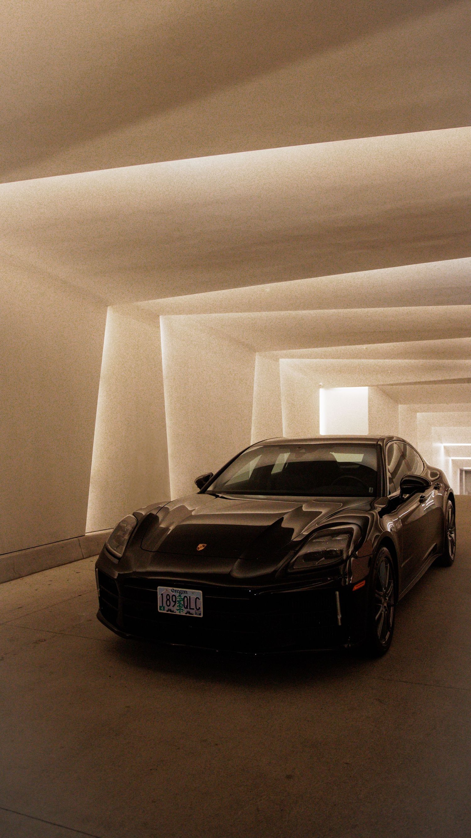 A sleek black Porsche sports car parked in a minimalist concrete tunnel with dramatic lighting and geometric lines.