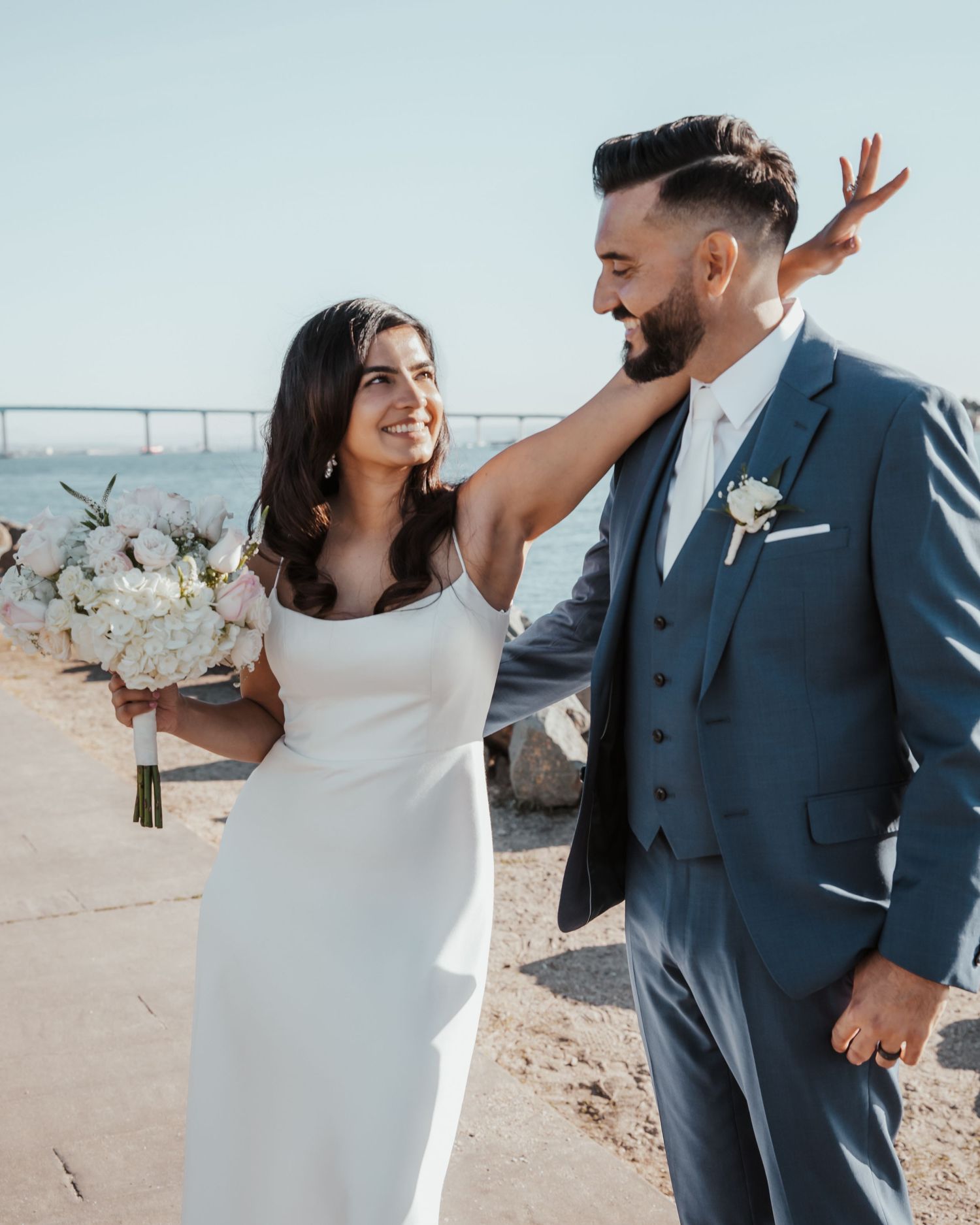 Romantic wedding photo shoot against a bright sky with white floral bouquet.