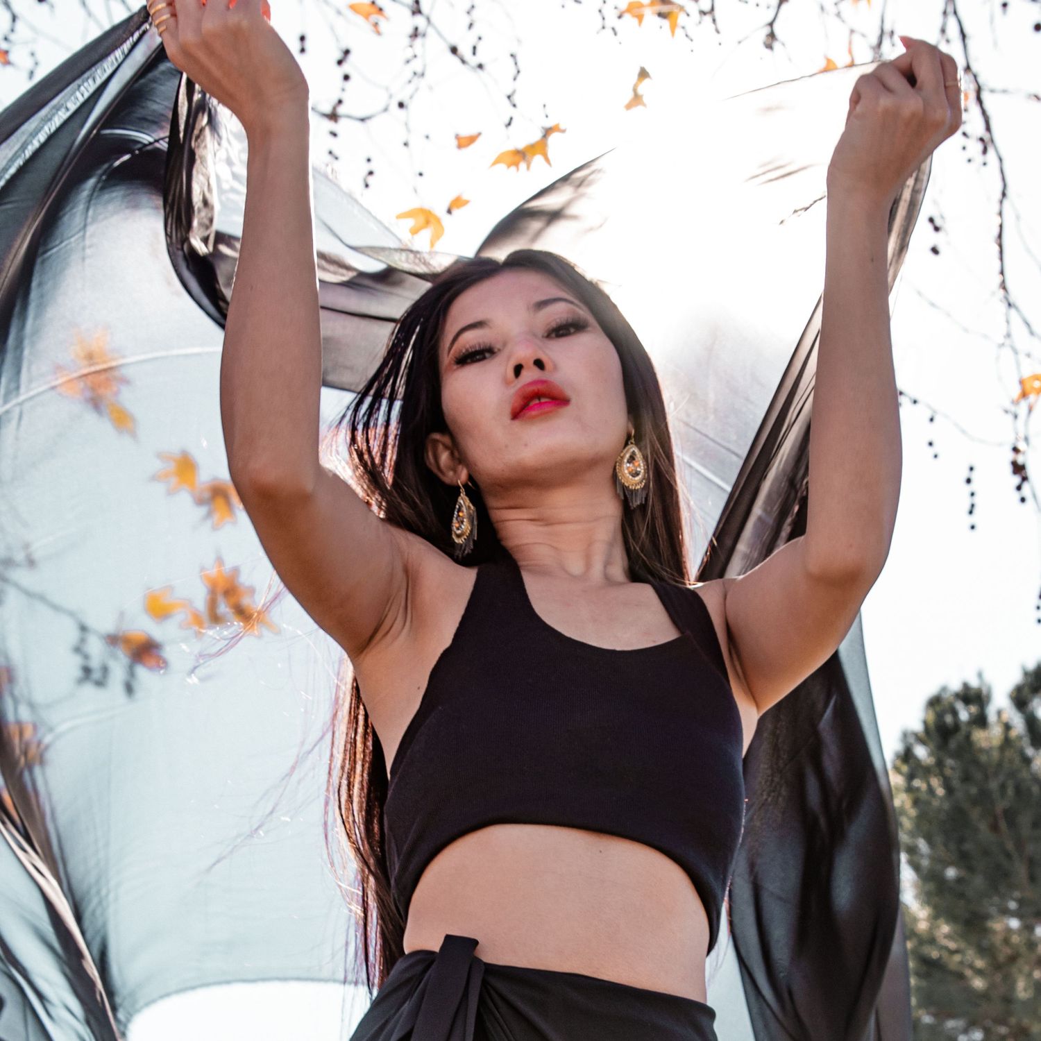 Woman in black athletic wear dances expressively with autumn leaves in background.