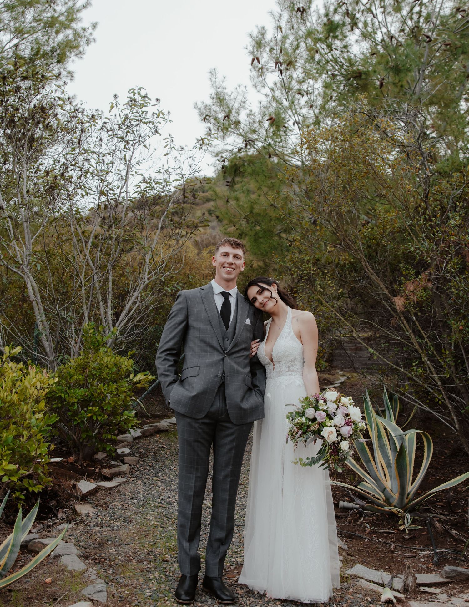 Wedding couple poses in garden setting with desert plants and natural landscaping.