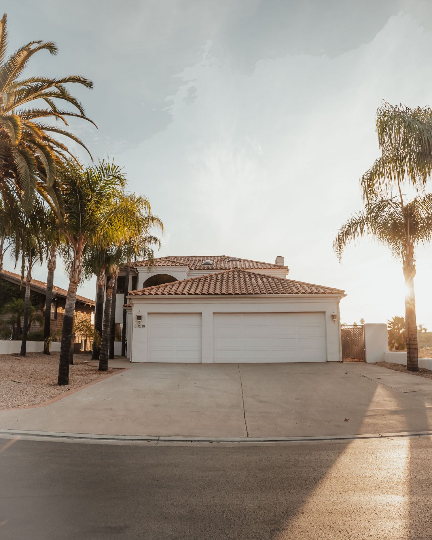 Mediterranean villa with white stucco exterior and palm trees at golden hour.