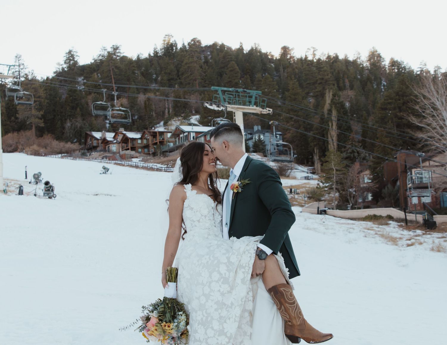 A couple shares a romantic moment on a snowy ski slope with chairlifts and winter scenery in the background.
