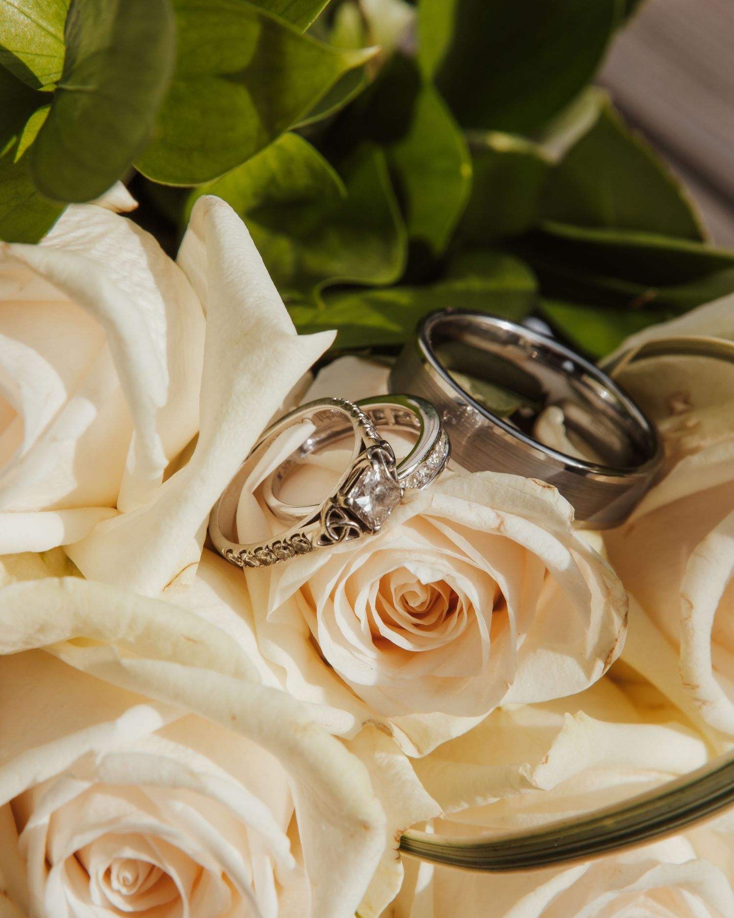 Close-up of delicate white roses with wedding rings nestled among the petals.
