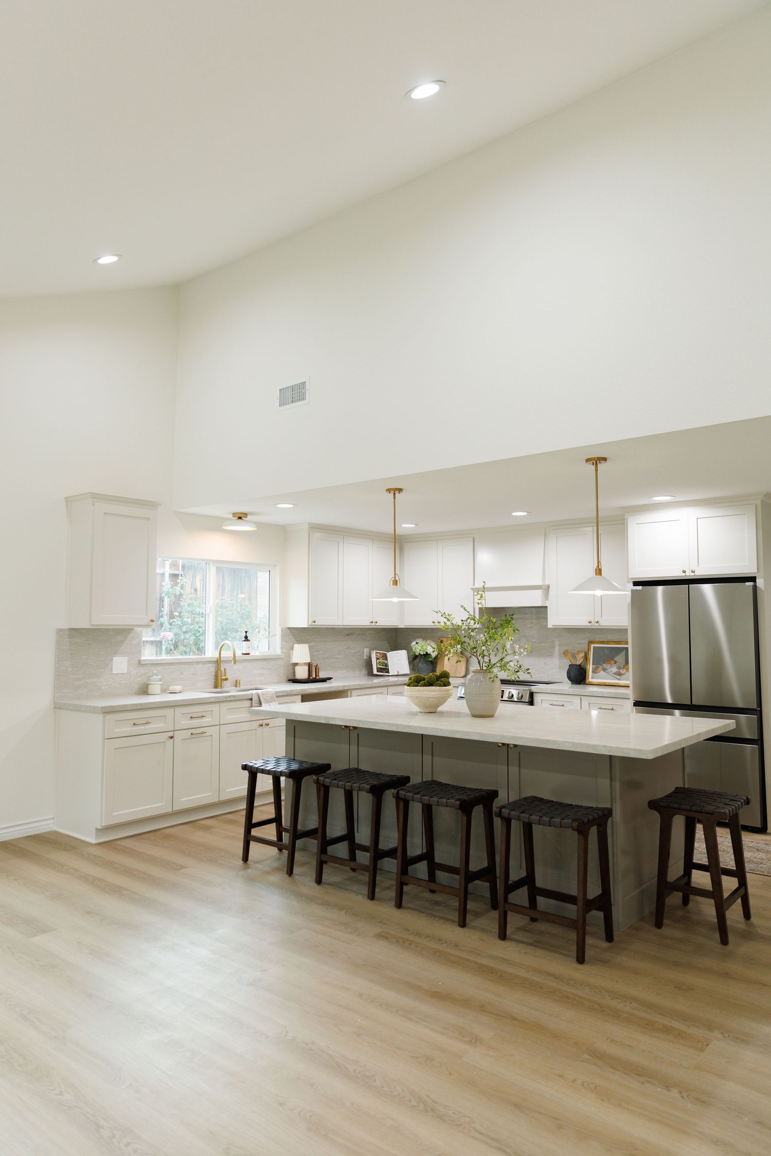 Modern white kitchen with large island, pendant lights, stainless appliances and light wood floors in contemporary design style.
