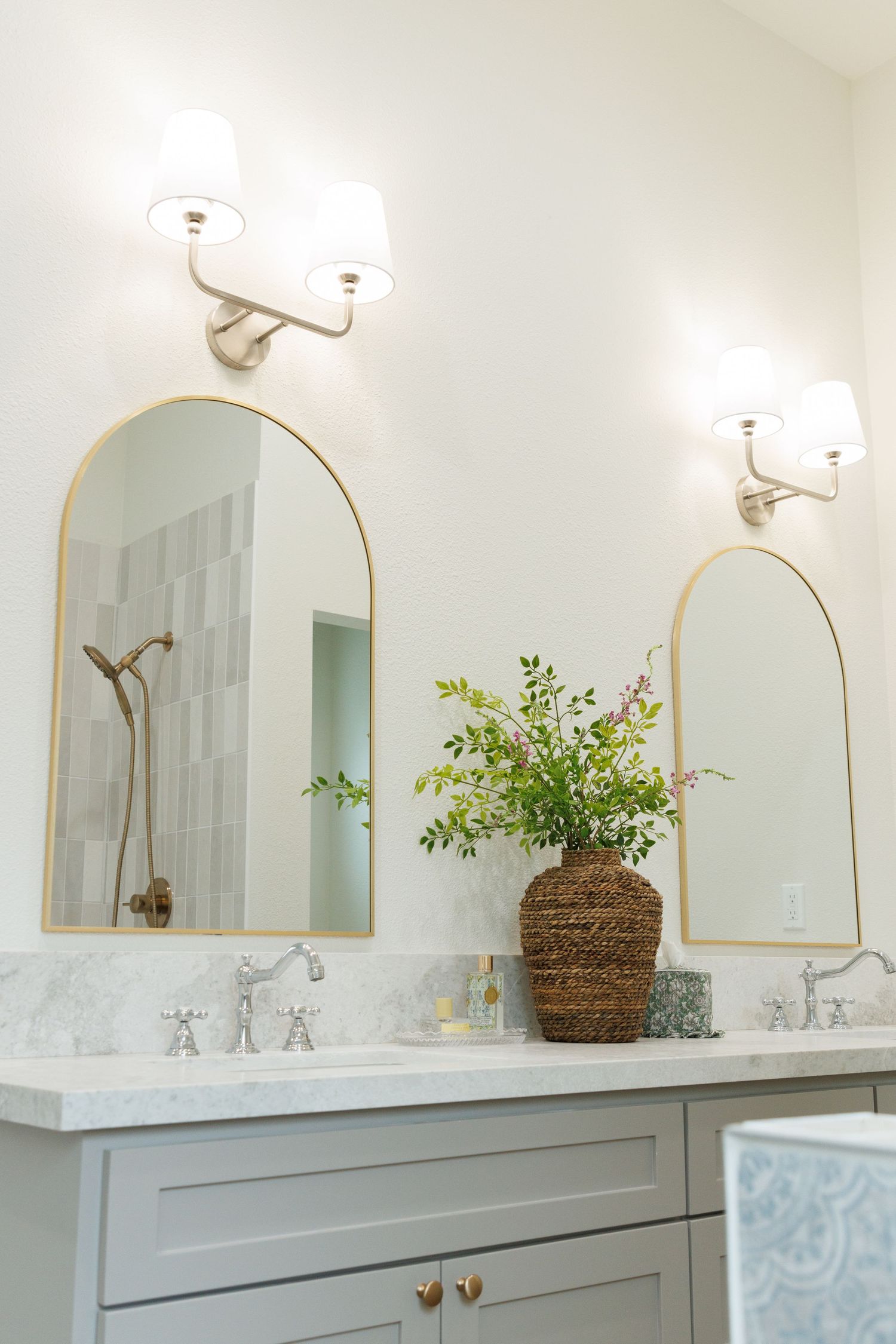 Modern white bathroom vanity with marble countertop, brass fixtures, and decorative woven basket with greenery.
