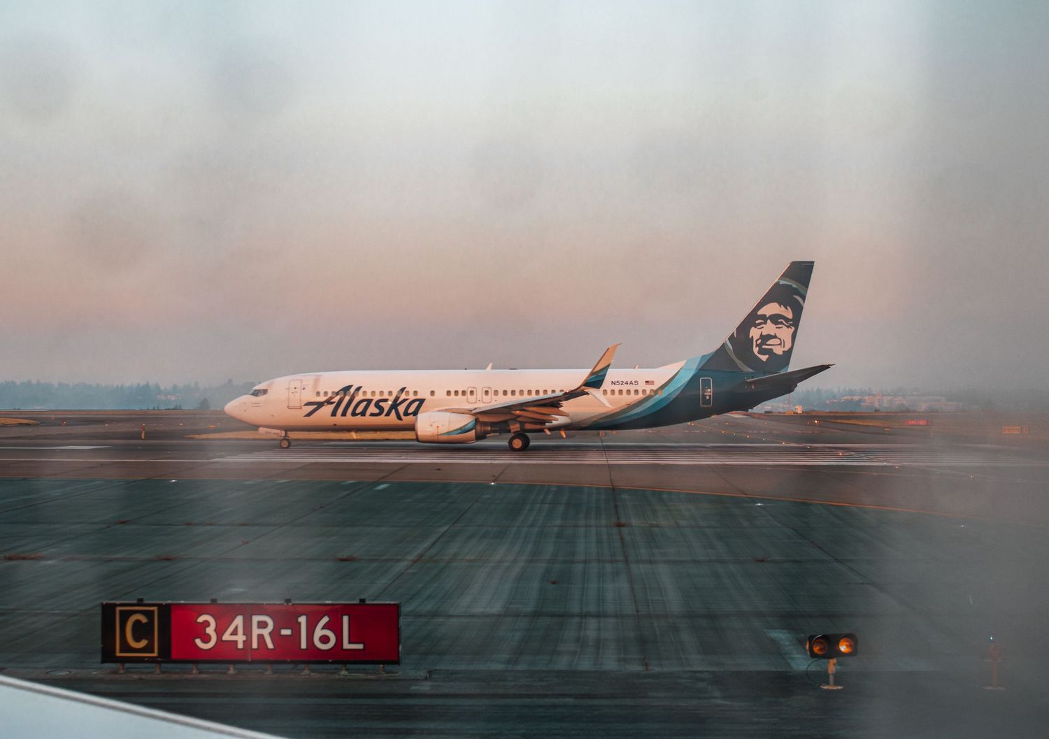 Alaska Airlines passenger plane taxiing on runway during sunset with gate marker visible.