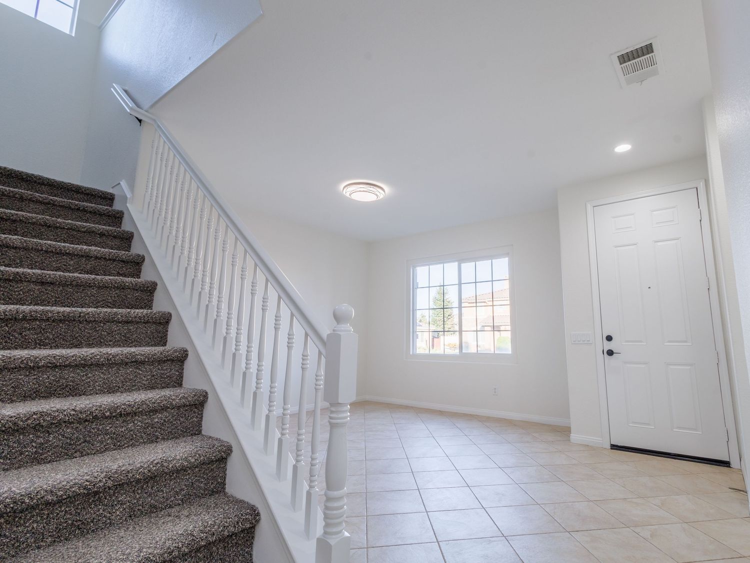 Modern white interior staircase with grey carpeted steps and natural lighting from windows.
