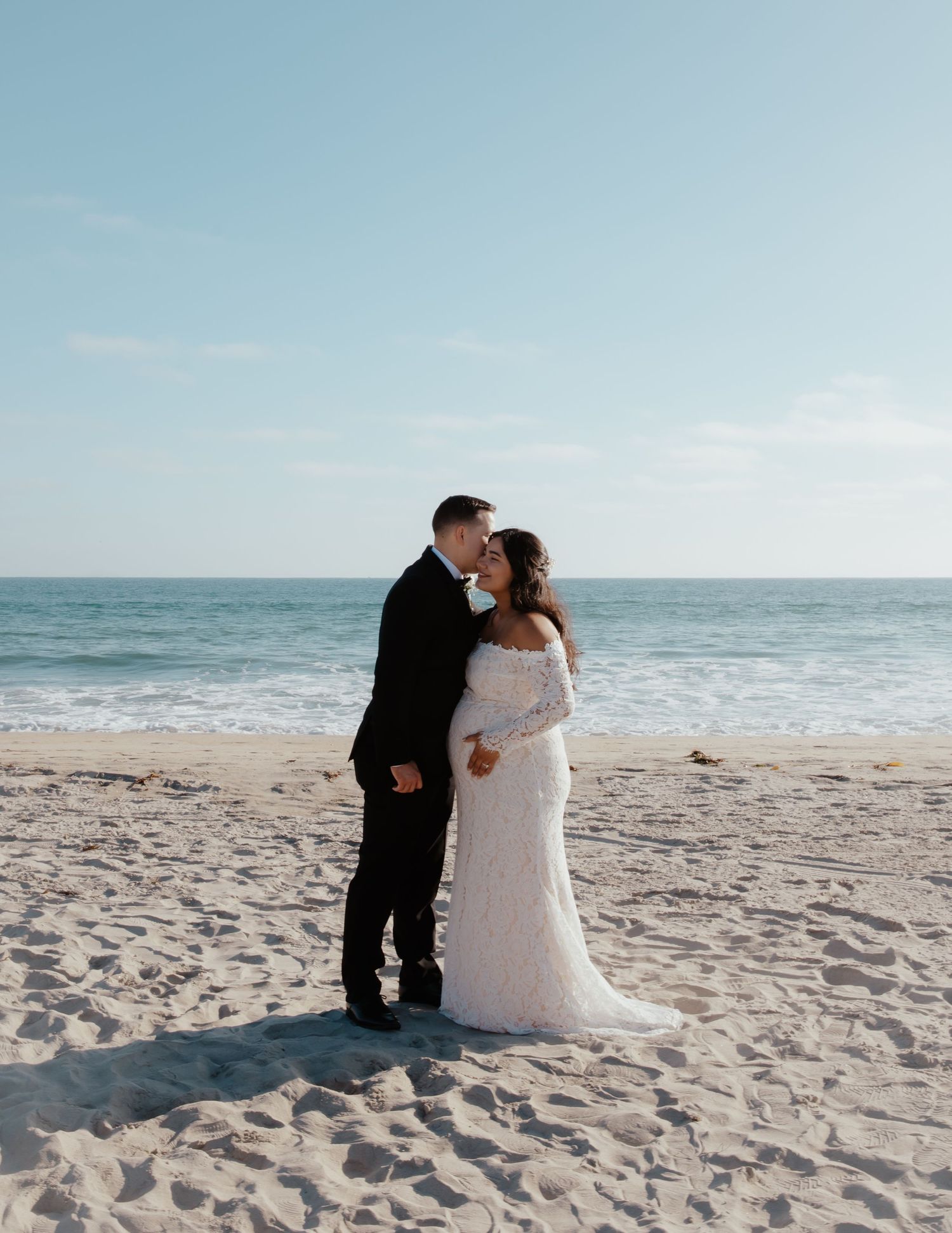 A romantic beach wedding photoshoot with a couple sitting together in the sand.