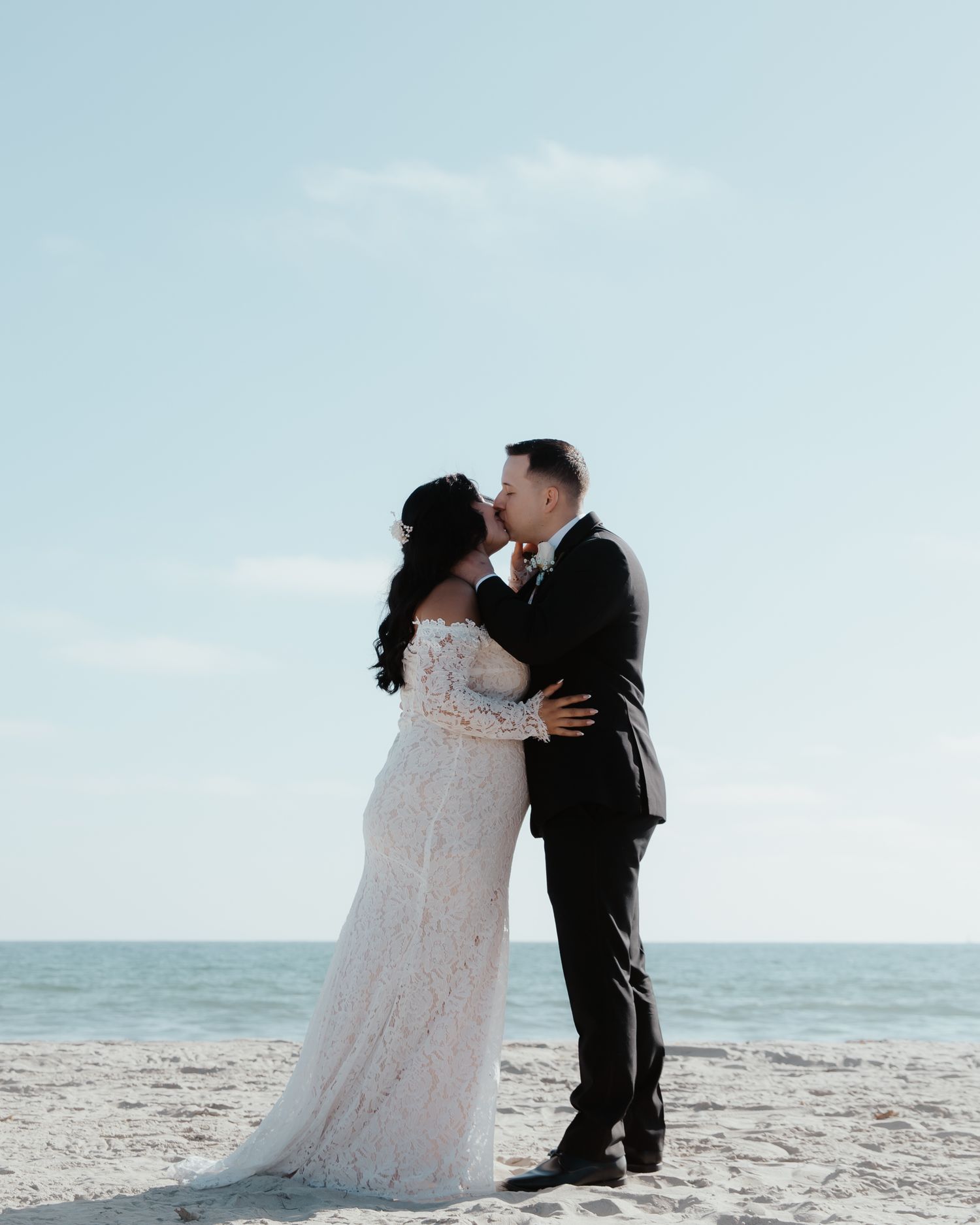 A couple shares an intimate moment on a sunny beach with the ocean in the background.