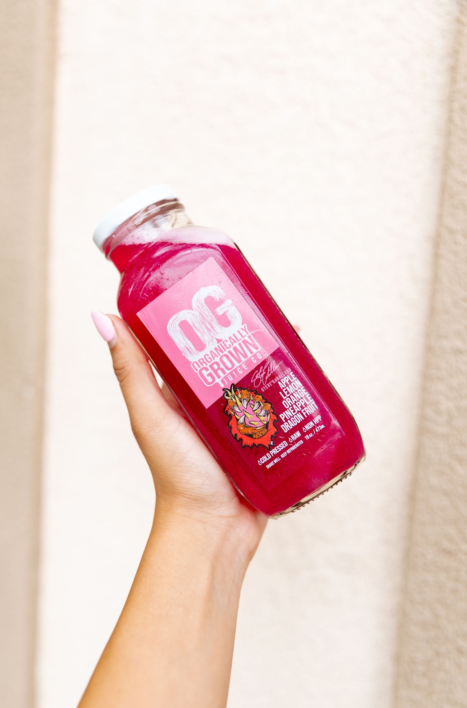 Hand holding pink beverage bottle against white background.