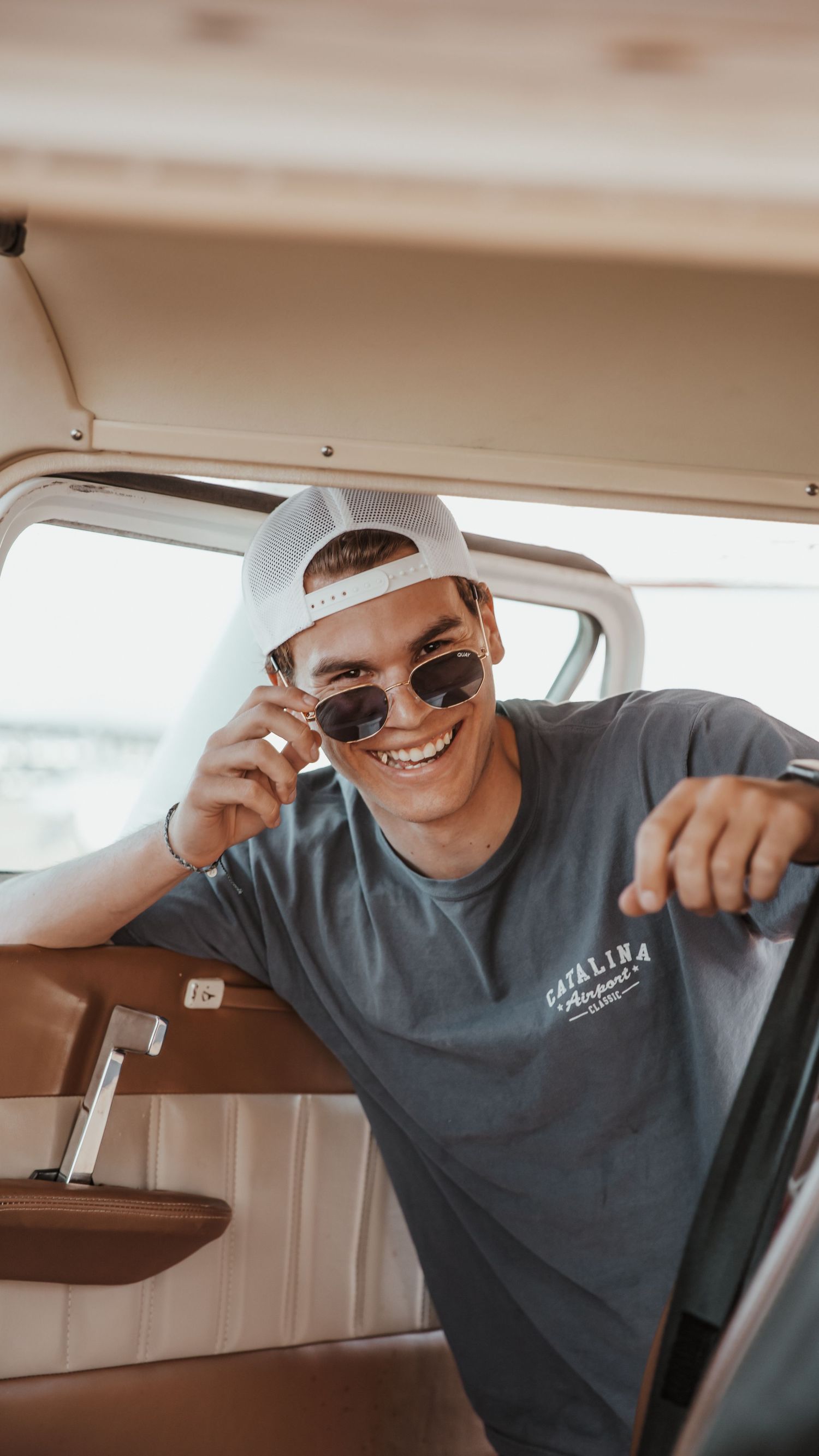 Person in a gray t-shirt playfully adjusting sunglasses while sitting in a car interior.