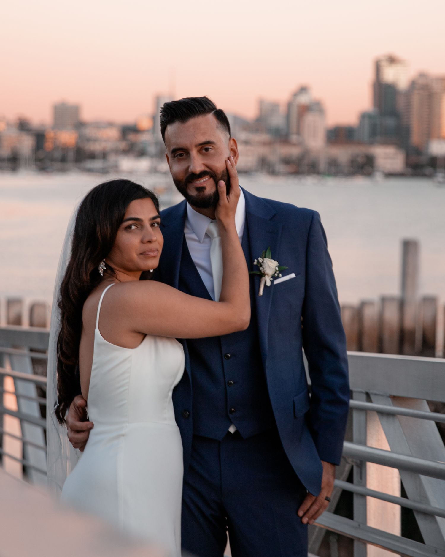 Sunset wedding portraits on waterfront deck with pink sky and city views.