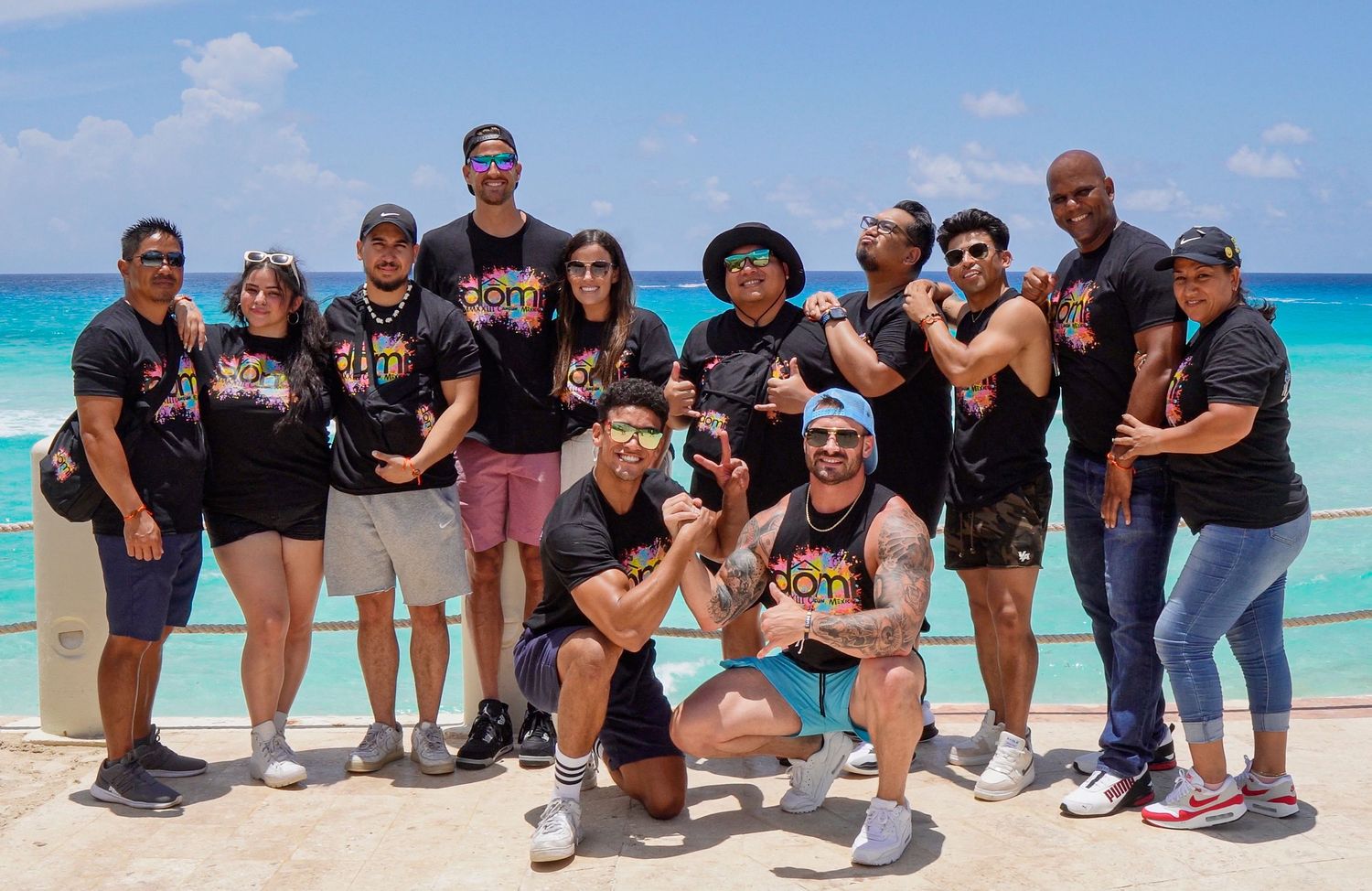 Large group poses together on a beautiful tropical beach with turquoise water in the background.