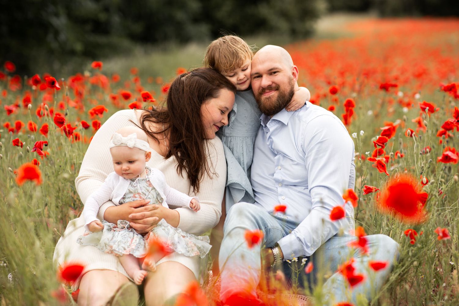 Familjefotografering i Skåne på ett vackert vallmofält. Familjen sitter ner bland vallmon och kramar kärleksfullt om varandra.