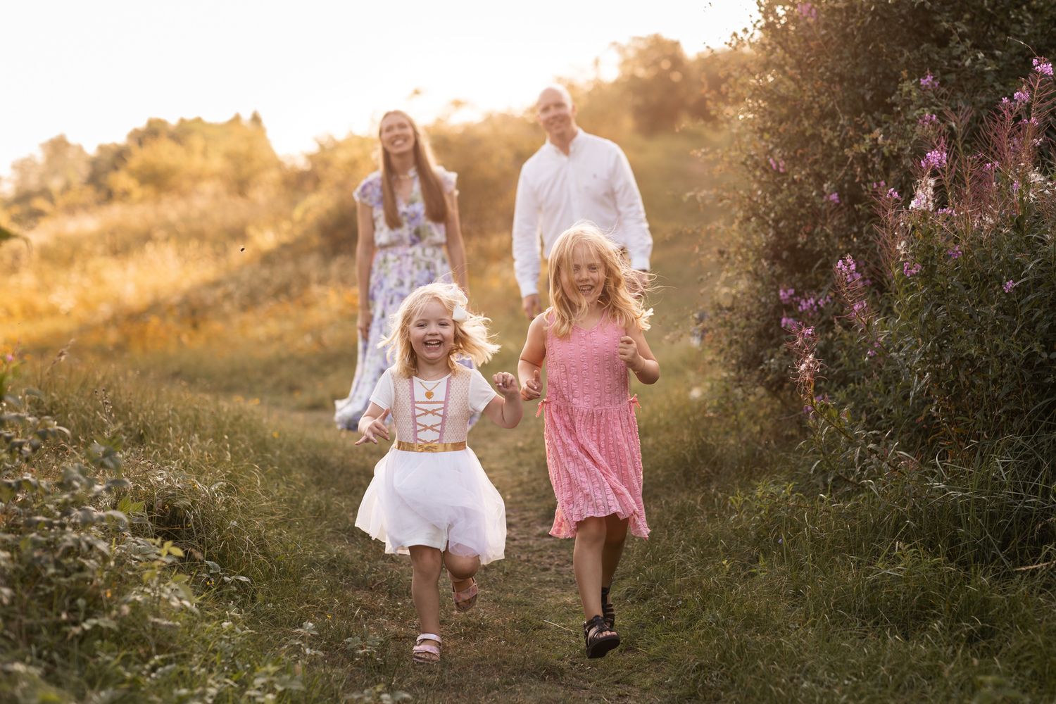 Familjefotografering en solig kväll nära Landskrona. Två barn springer glatt och lekfullt mot kameran och ler stort. De busar med fotografen