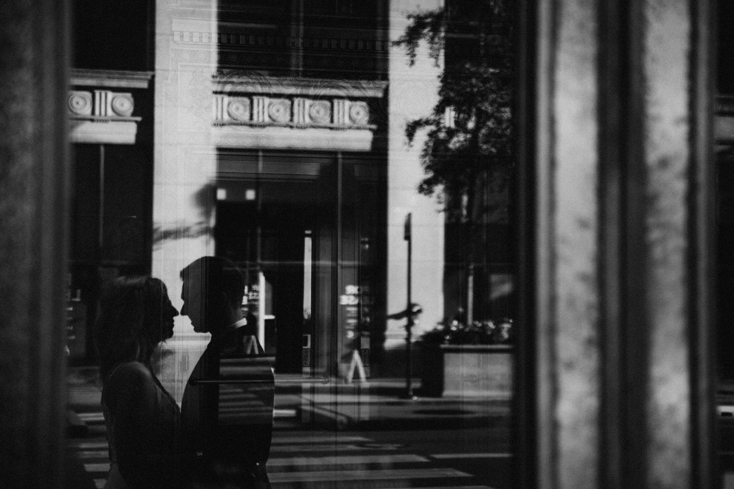 Reflection of a bride and groom about to kiss in a window, with architectural details and street scene near City Hall; artistic Chicago wedd