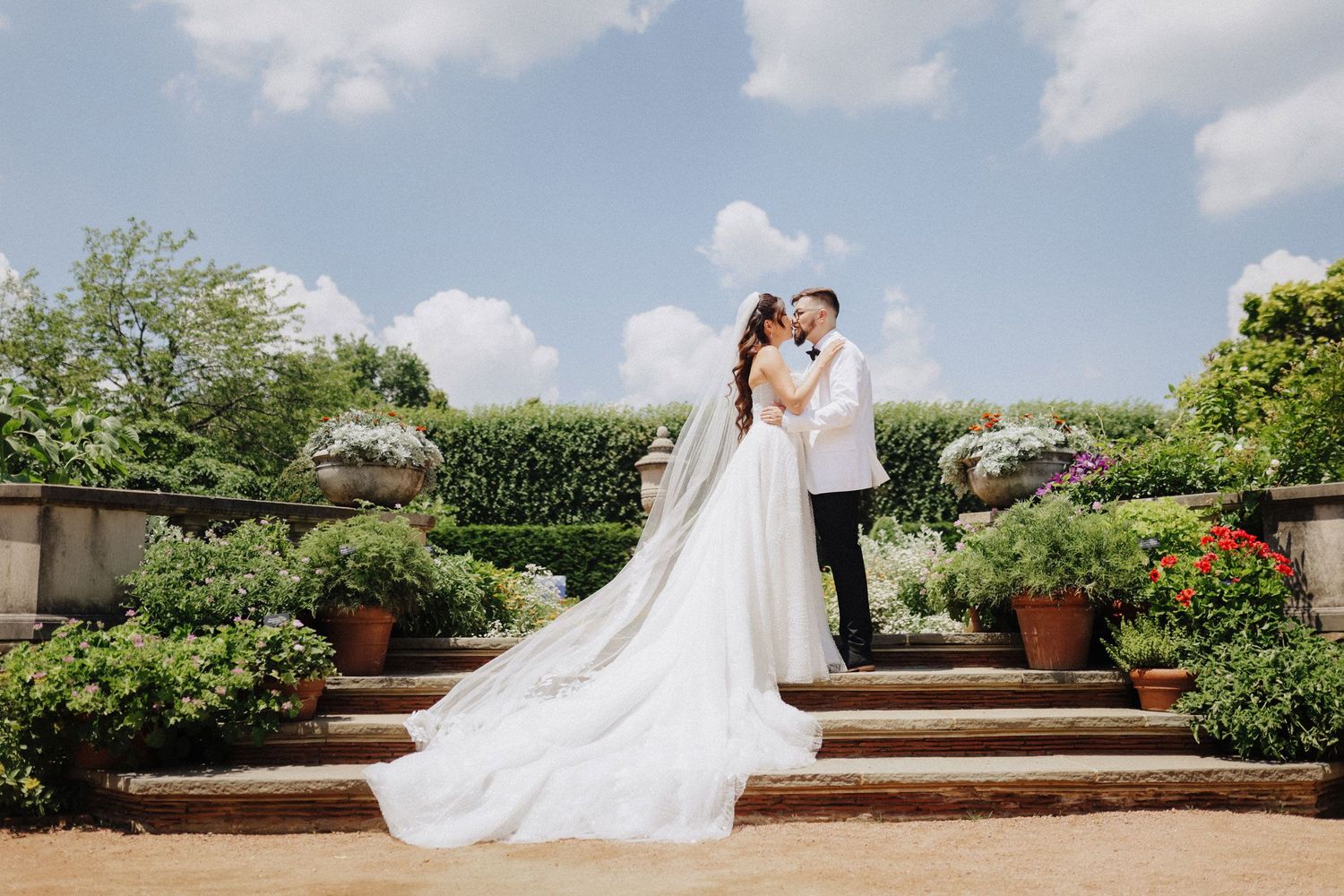 Bride and groom embracing on garden steps at Chicago Botanic Garden, surrounded by lush greenery and flowers; elegant outdoor wedding portra