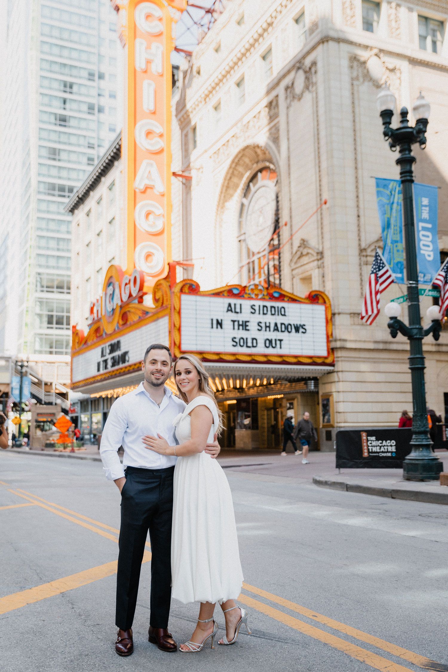 Engaged couple posing in front of the iconic Chicago Theatre marquee on a sunny day in downtown Chicago.