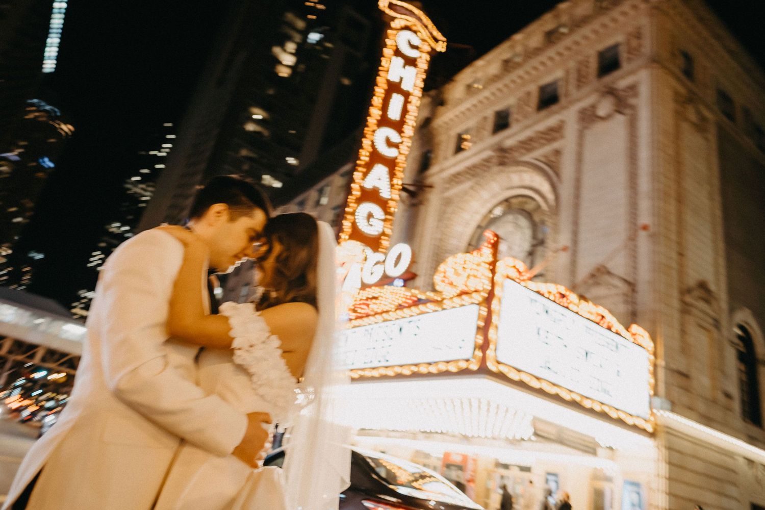 A bride and groom embrace in front of the illuminated Chicago Theatre marquee at night, captured perfectly by a skilled wedding photographer