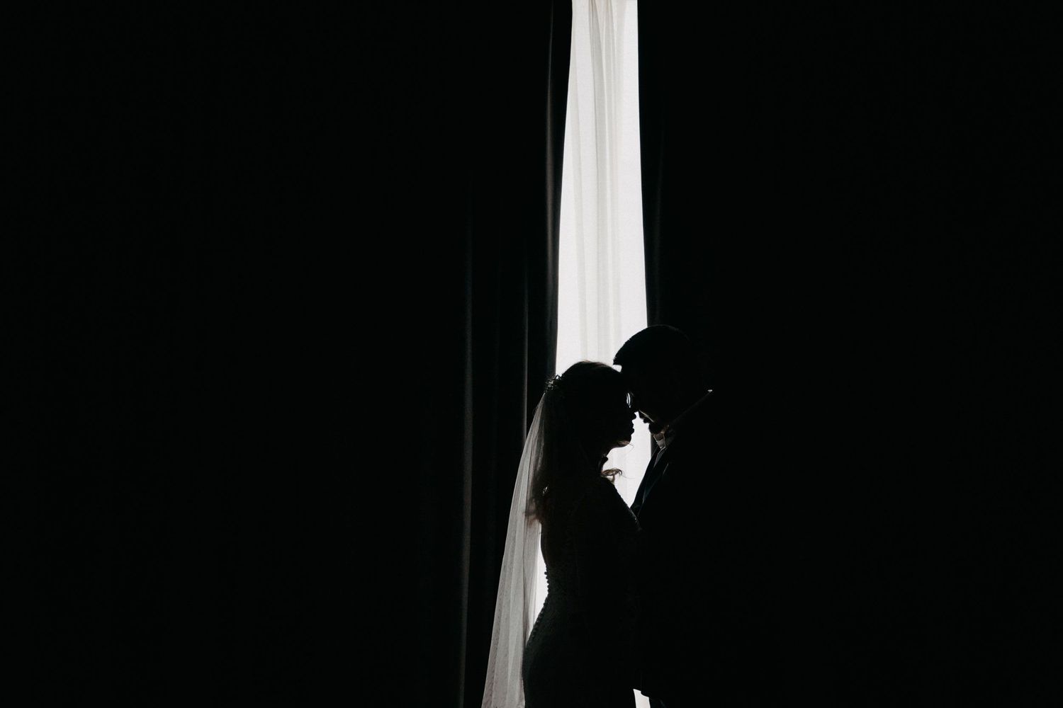 Silhouette of bride and groom touching foreheads in front of a bright vertical light strip; dramatic Chicago wedding photography style.