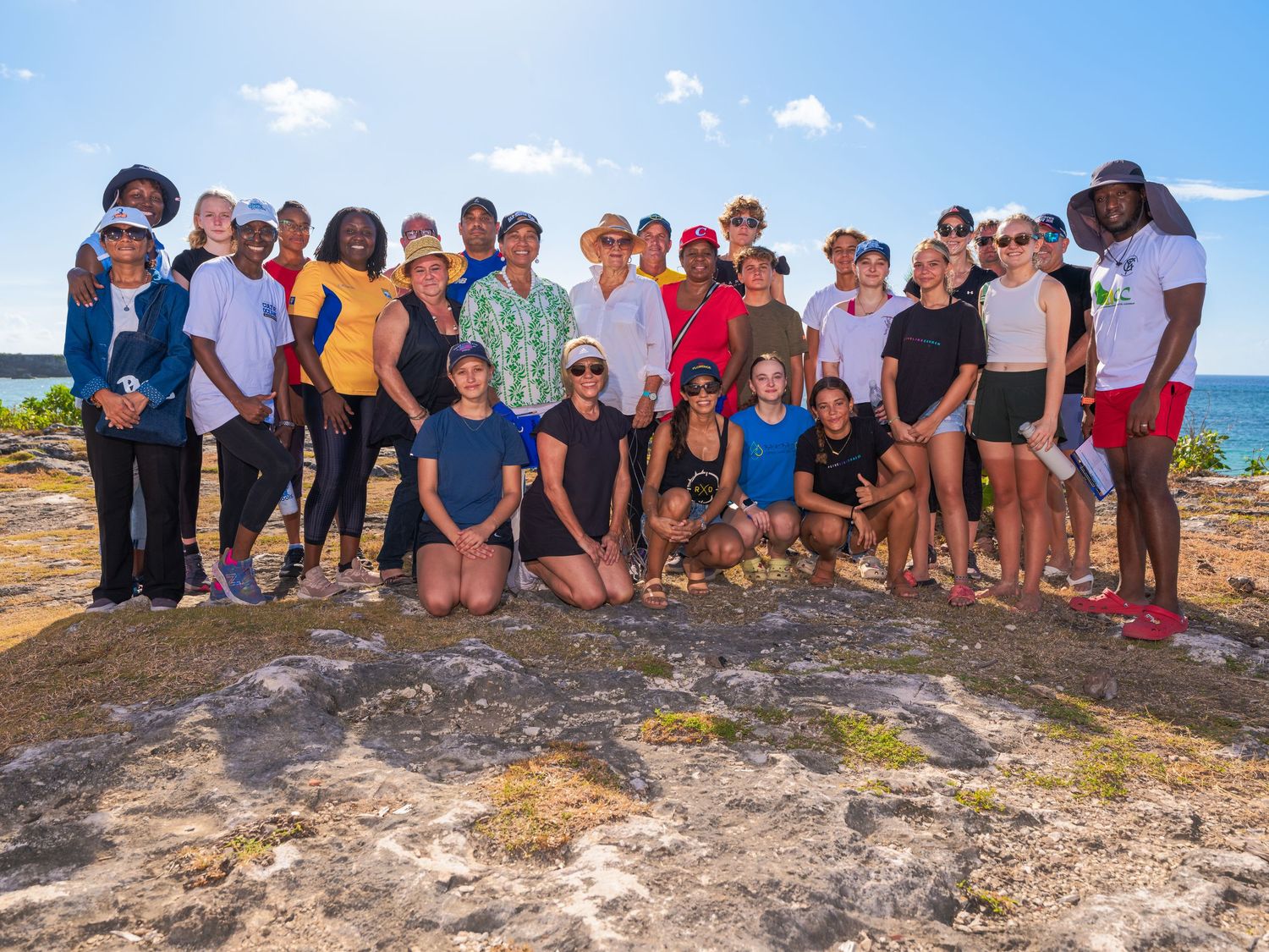 Group portrait outdoors in Barbados during event photography session, featuring diverse participants with clear sky and sea in background