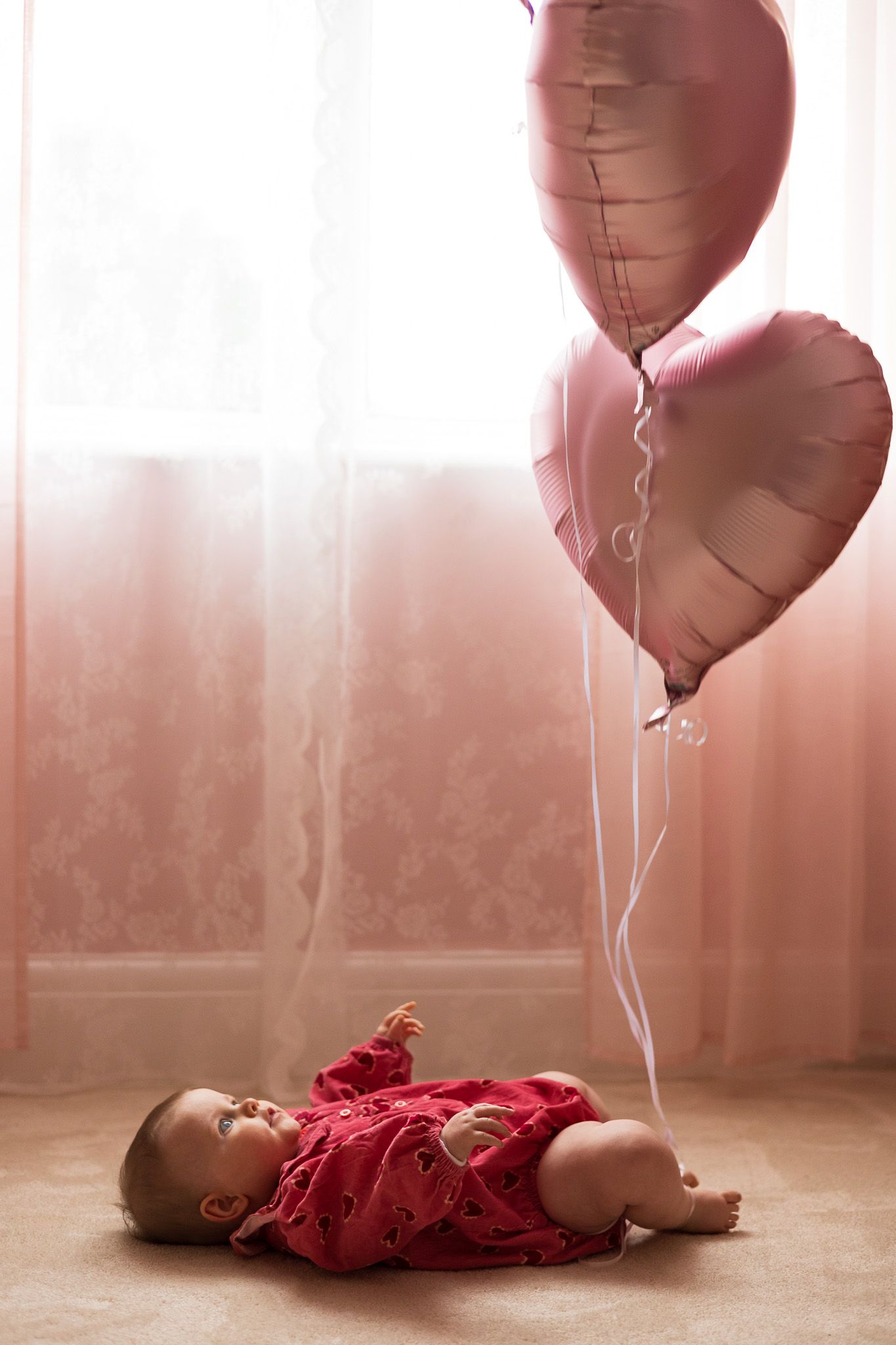 Baby lying beneath a heart-shaped balloon in a red outfit