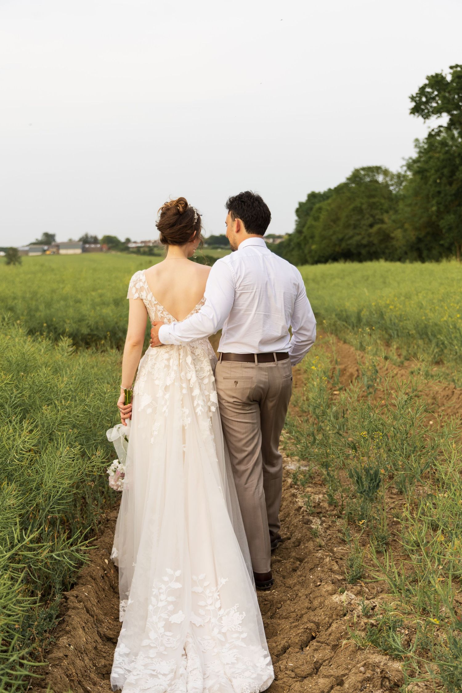 Bride and groom walking away hand in hand through a field