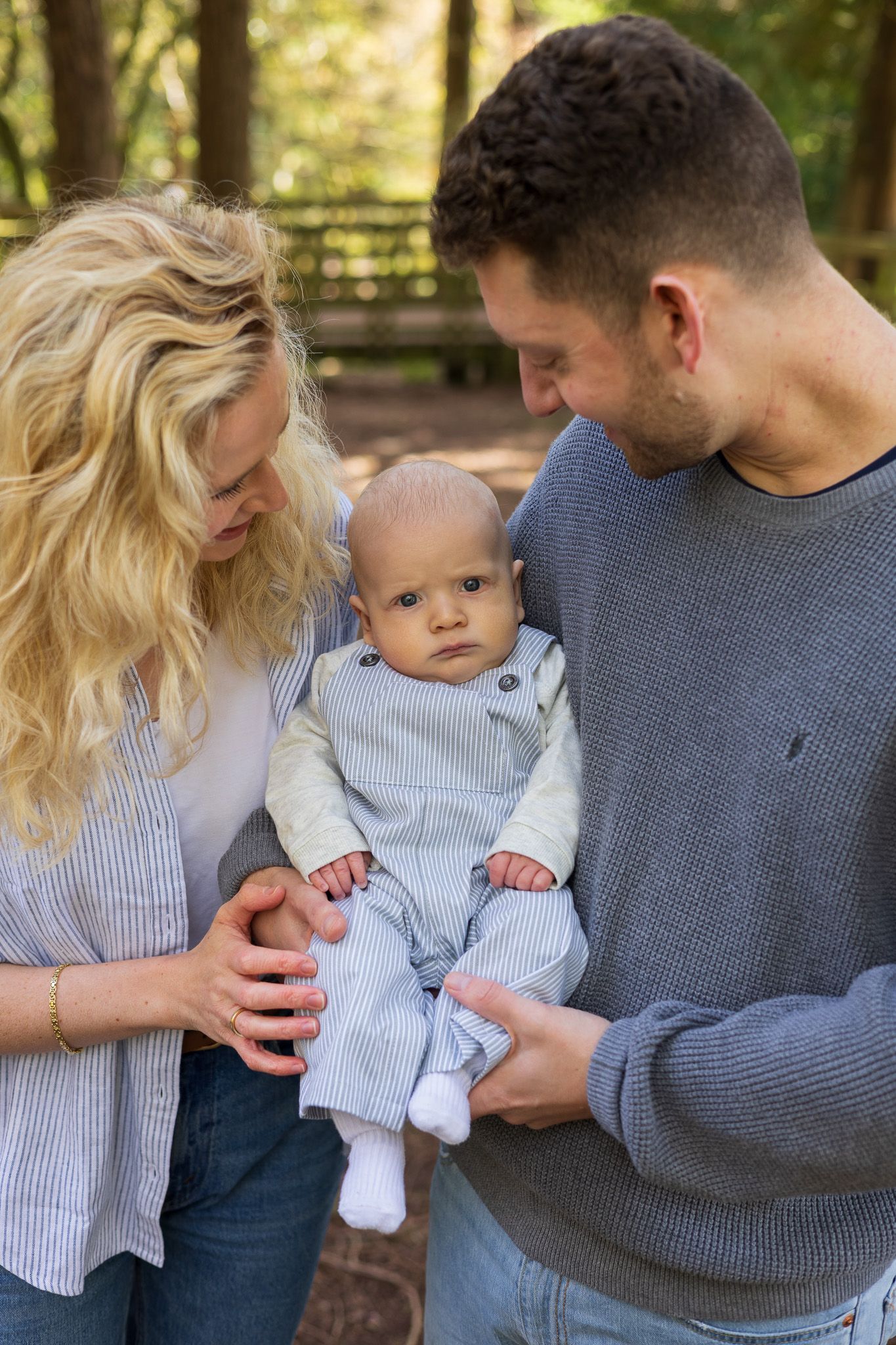 Parents holding their baby's hands as he stands between them outdoors