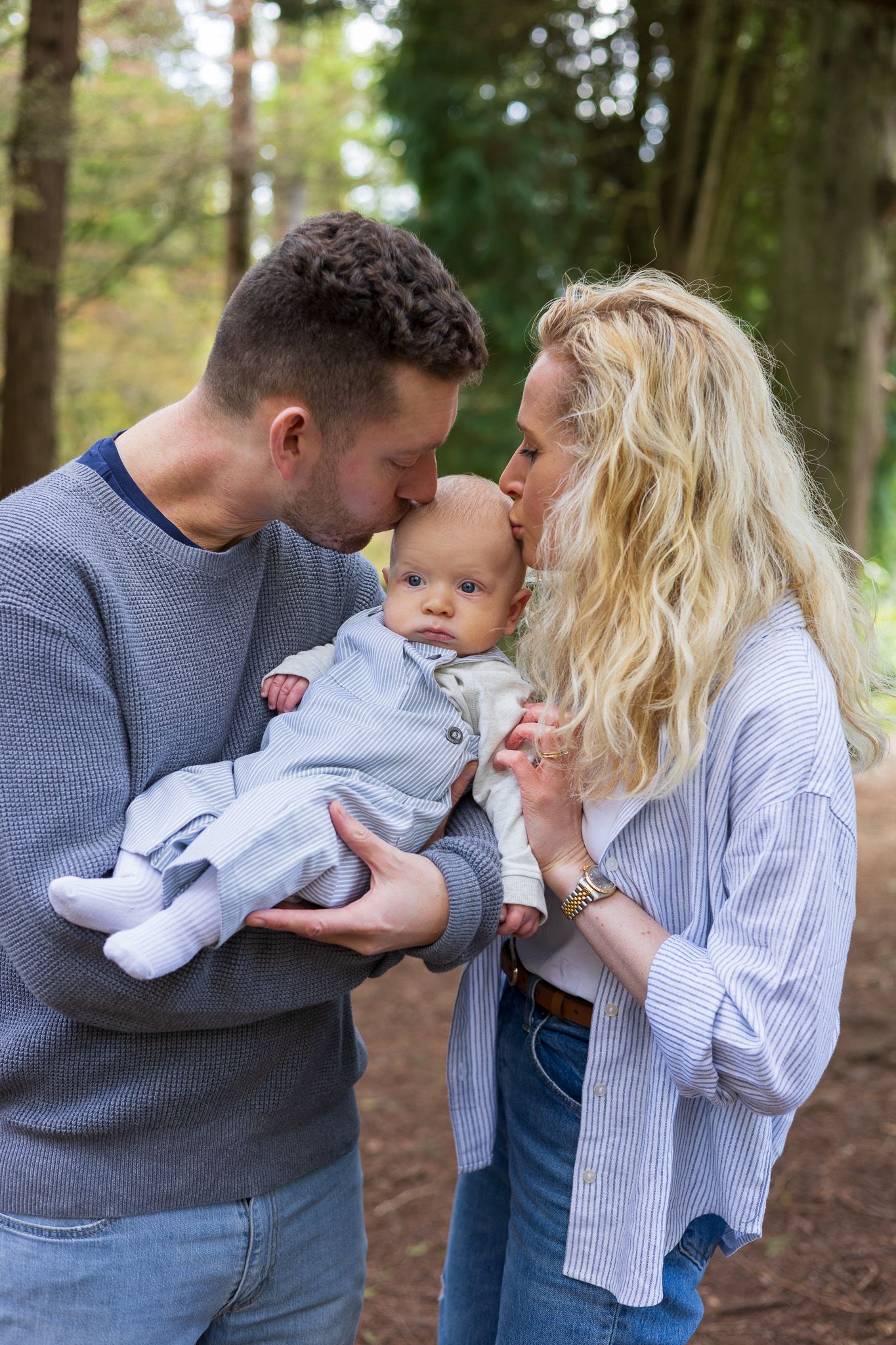 Parents holding their baby and smiling at the camera in a wooded setting