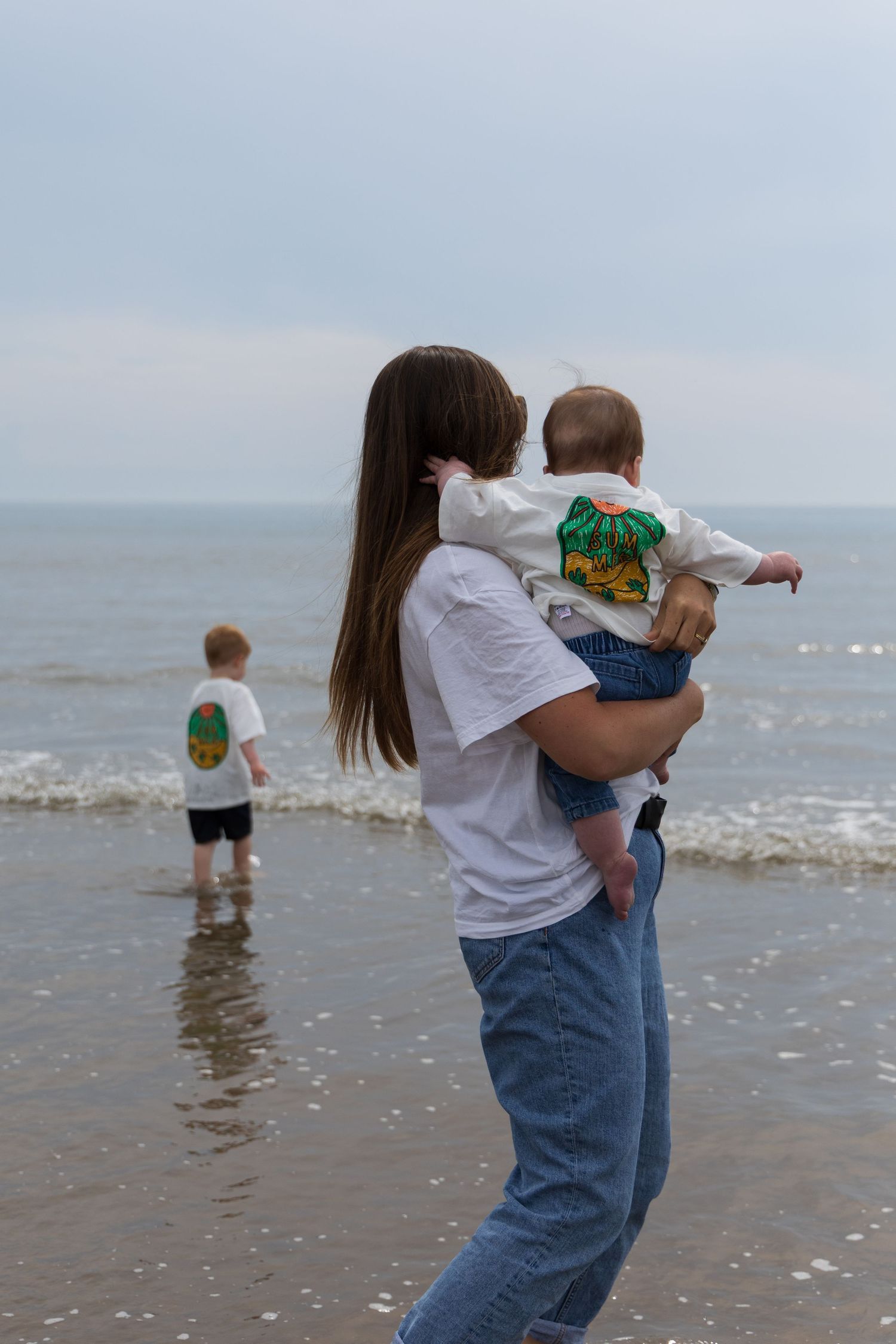 Mother holding her baby while standing in shallow water at the beach