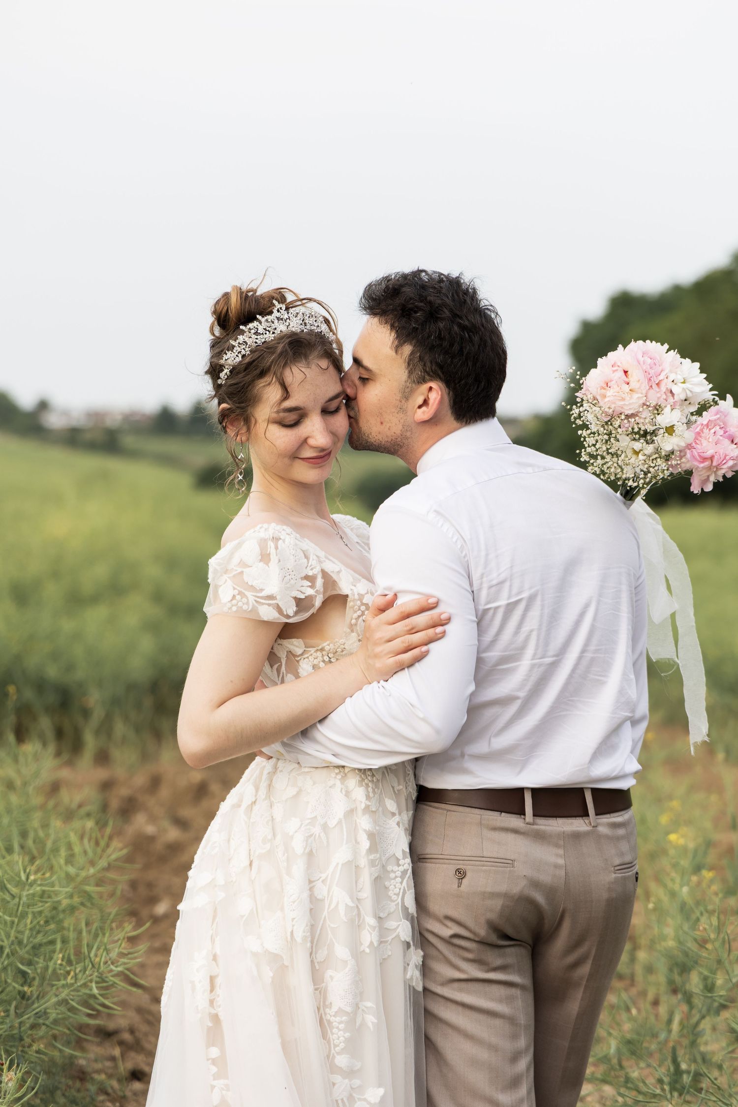 Couple embracing and kissing outdoors in a field holding flowers