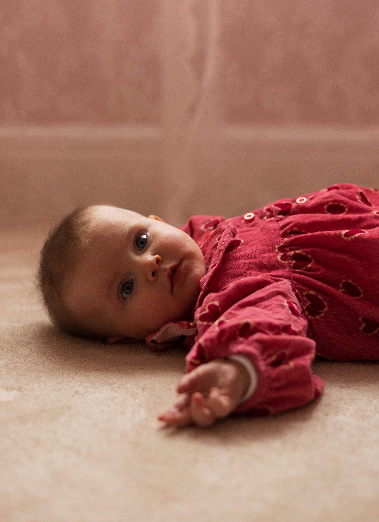Baby in a red outfit lying on the floor looking up at the camera