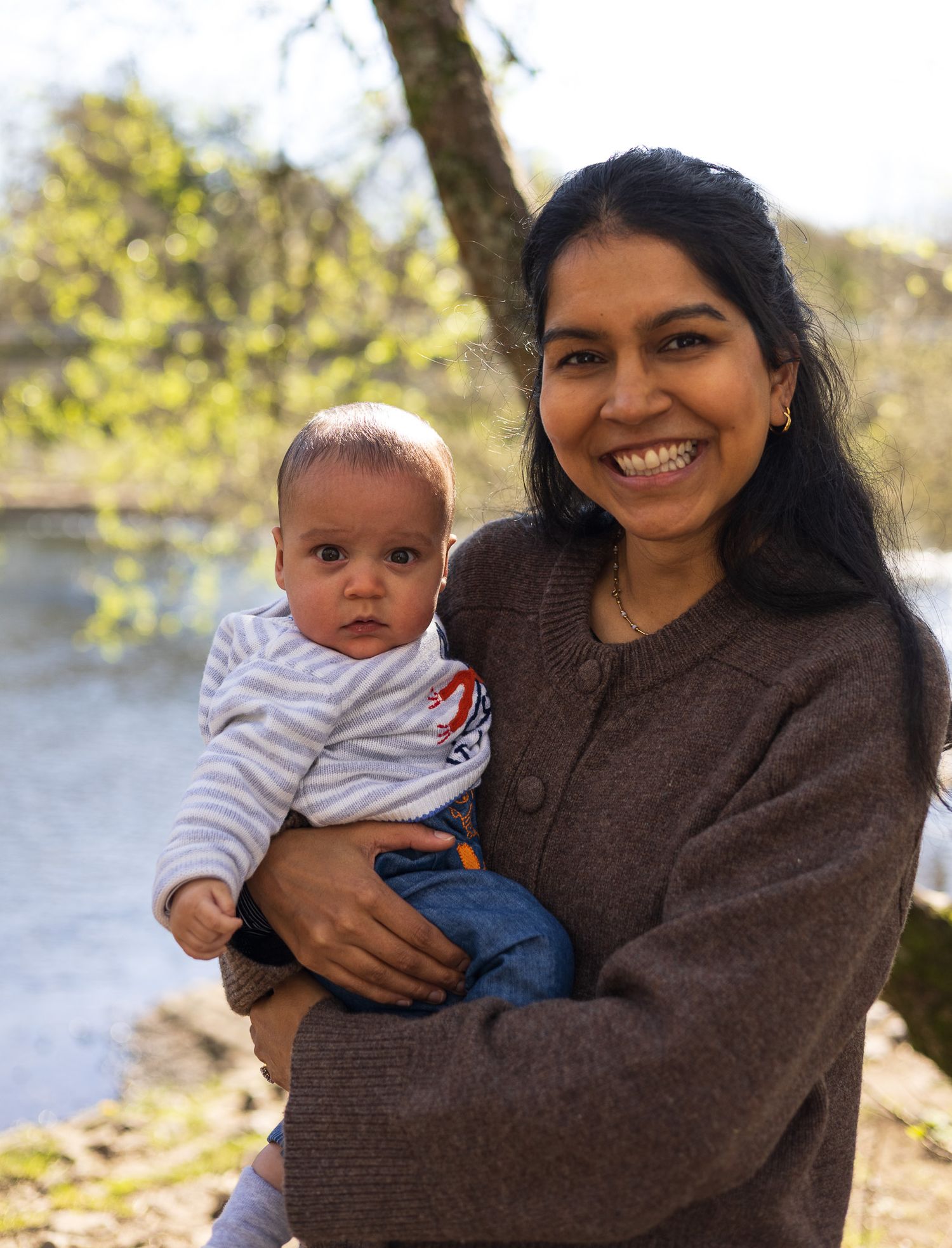 Mother smiling and holding her toddler outdoors by the water