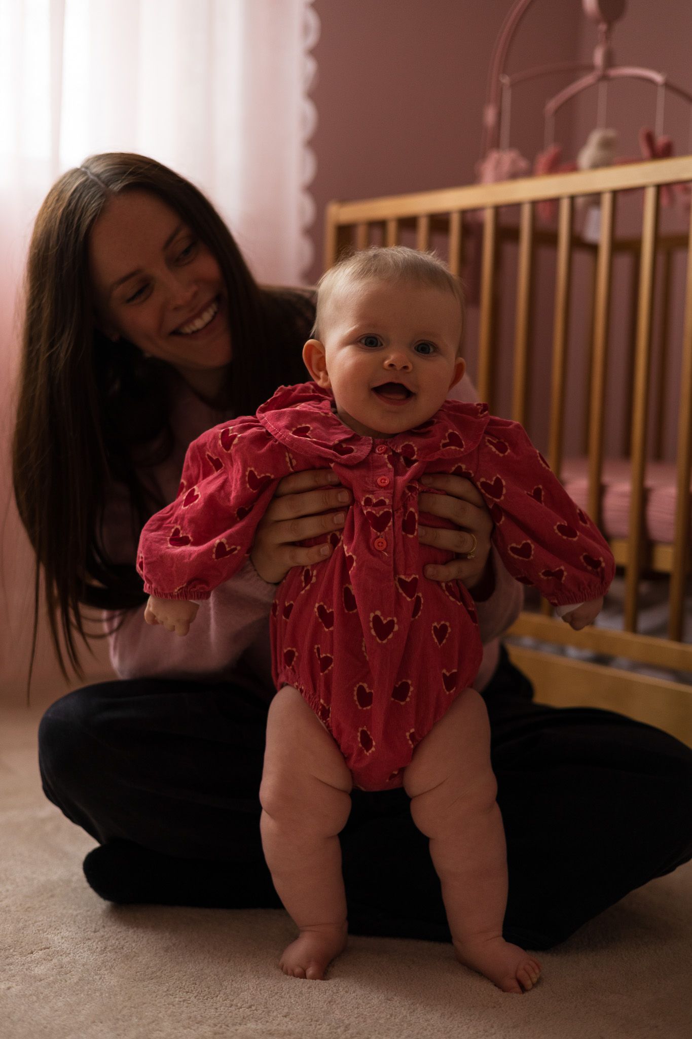 Mother holding her baby dressed in a pink knitted outfit in the nursery