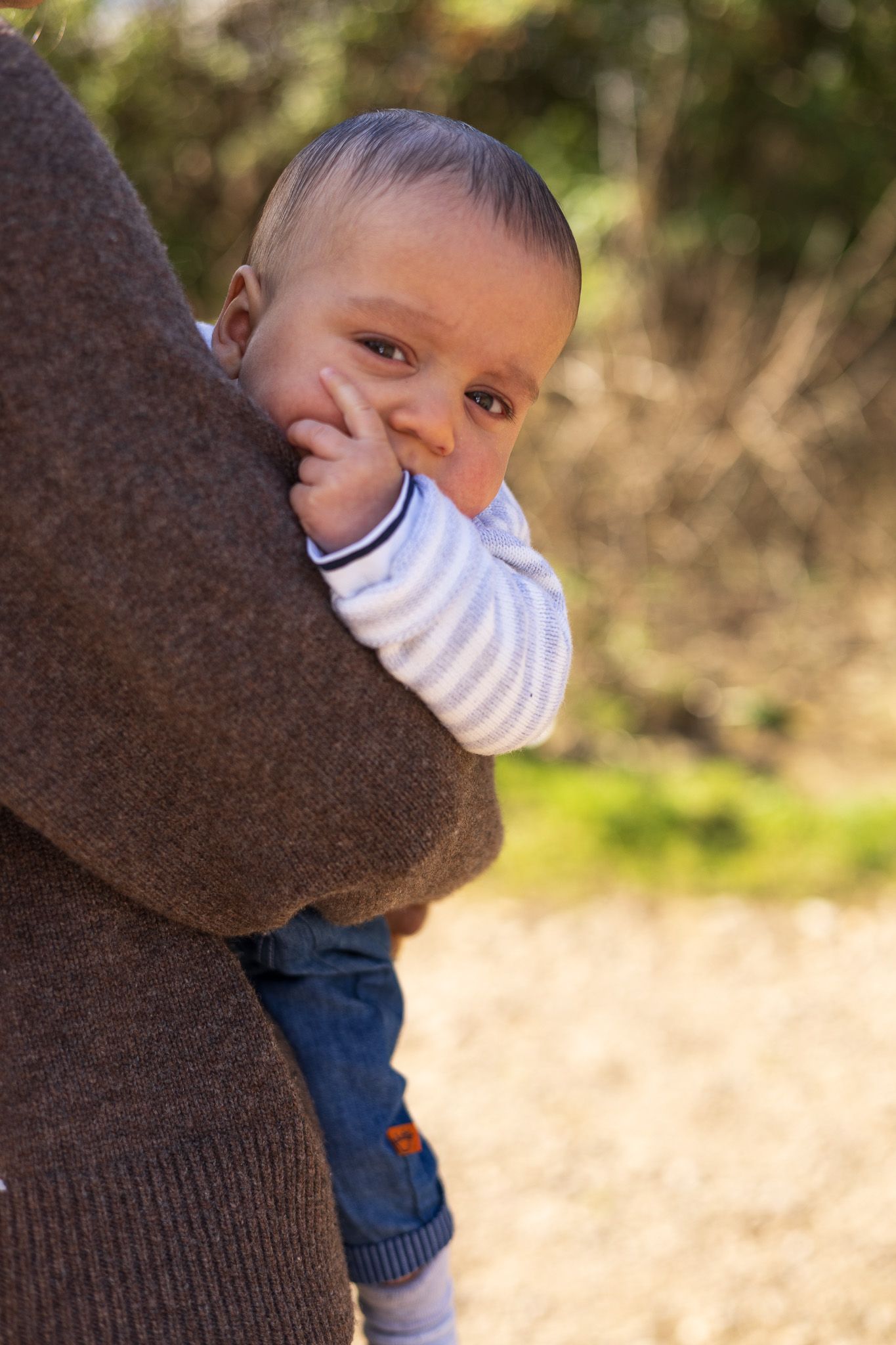 Smiling baby peeking over his mother's shoulder outdoors