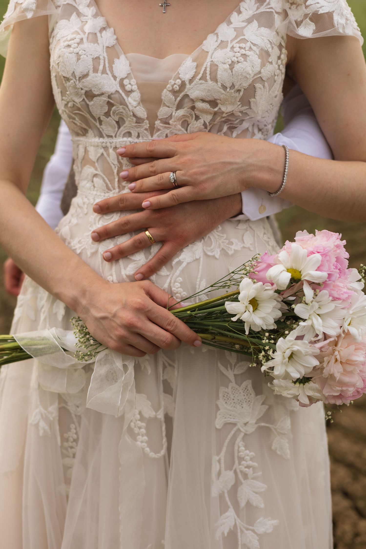 Close-up of bride's lace wedding dress and bouquet of pink flowers
