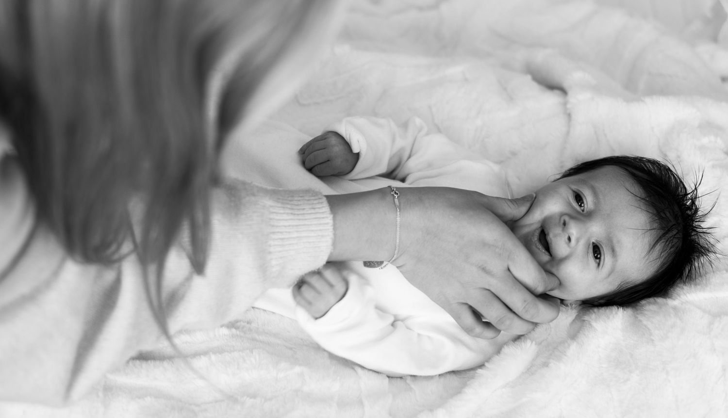Black and white photo of a mother laughing with her newborn baby on the bed